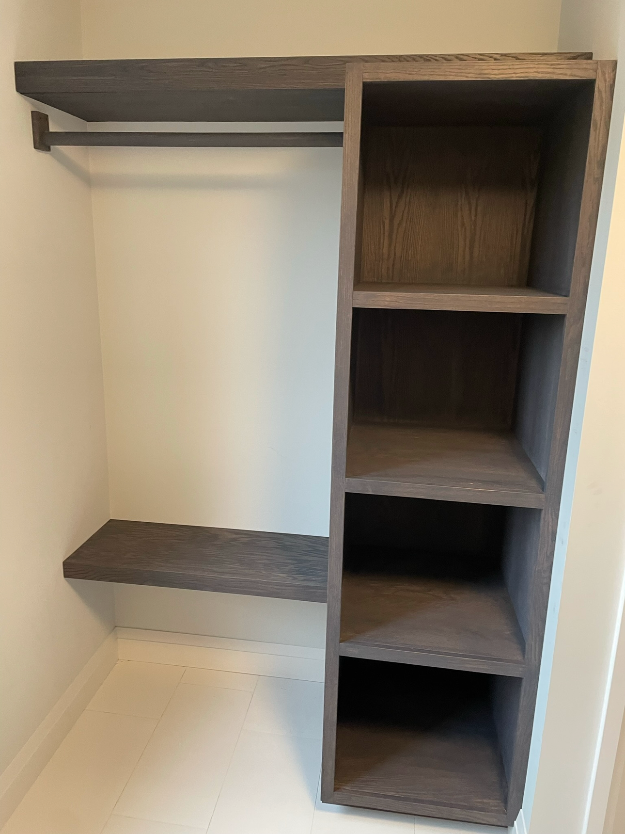 Empty walk-in closet with built in custom wooden shelves on the right and a hanging rod with a shelf above on the left.