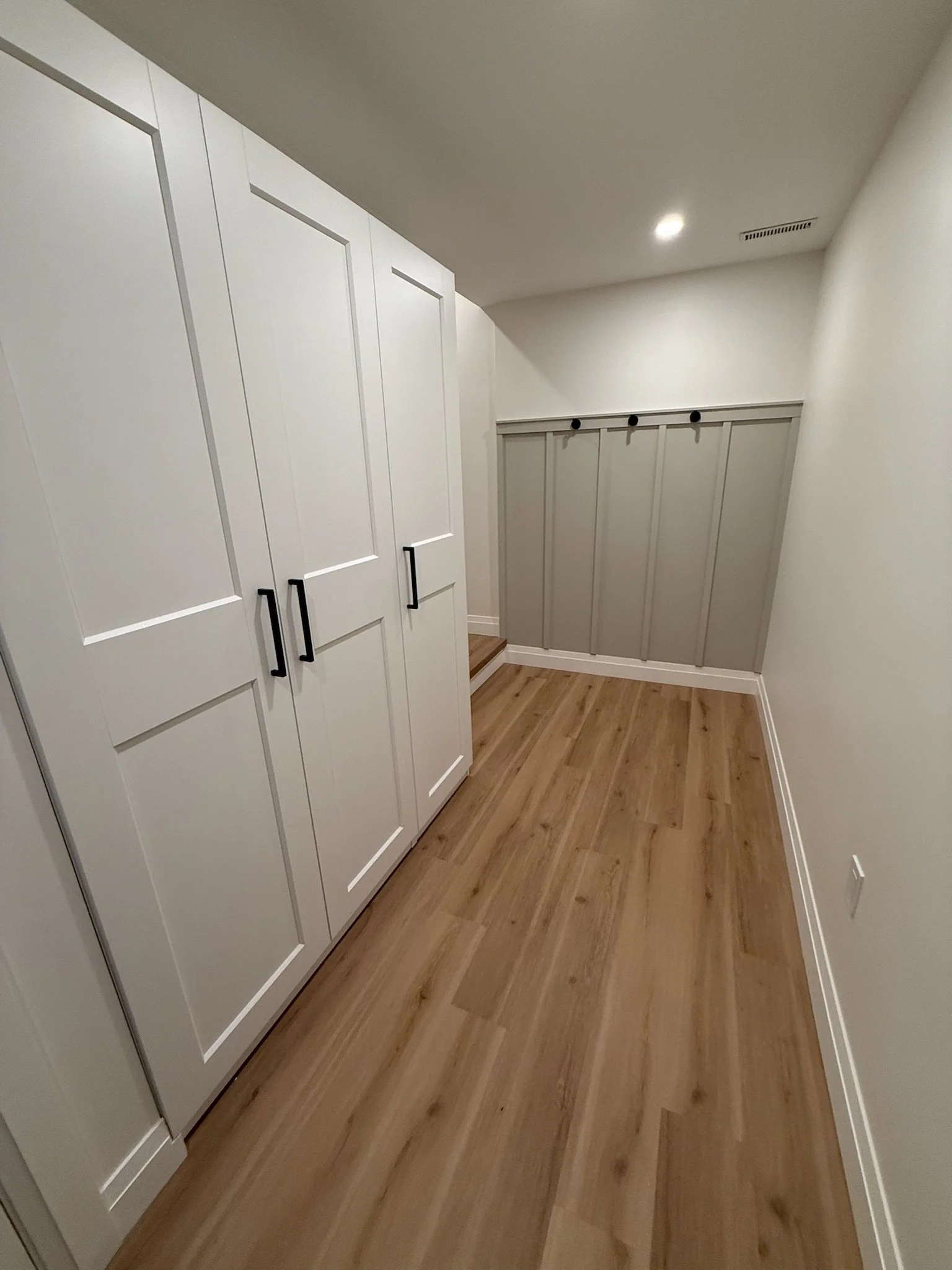 Interior of a room with white cabinets and wood flooring, with a staircase and a wall vent visible up close.