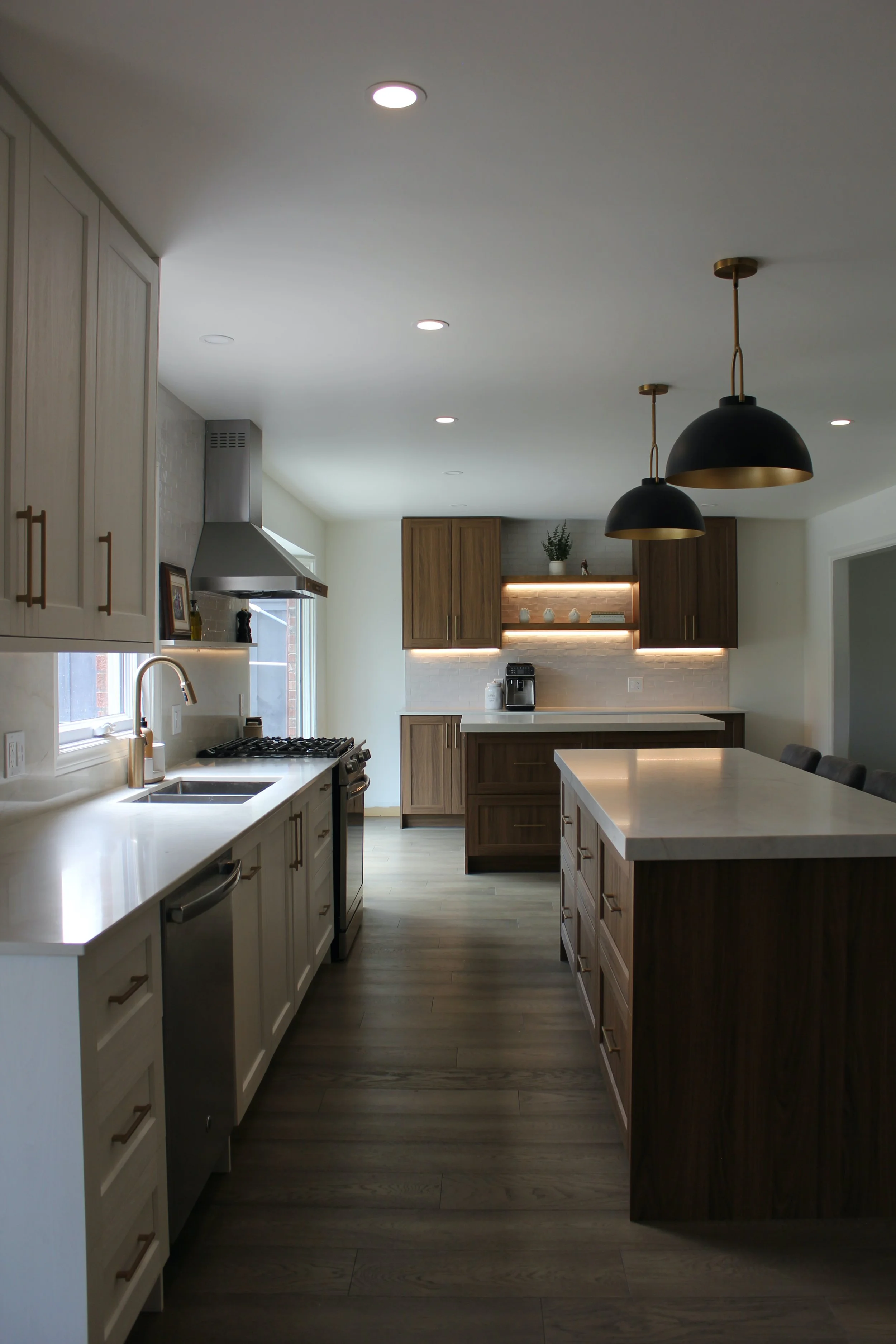 Modern kitchen with white cabinets, wood accents, black and gold pendant lights, and stainless steel appliances. Taj mahal quartz with mitered 2” island