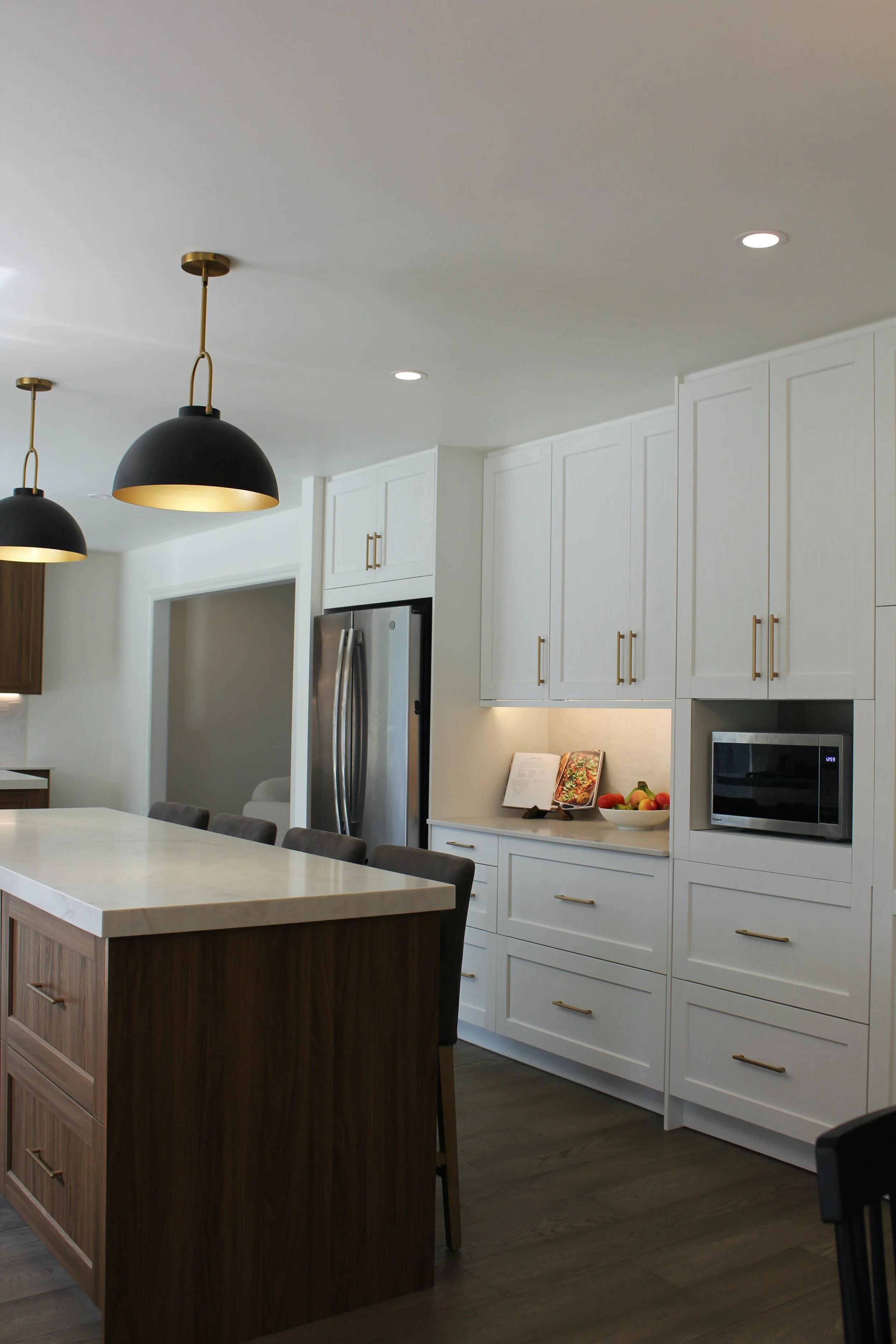 Modern kitchen with white cabinets, a built-in microwave, a refrigerator, black pendant lights, and a kitchen island with a marble top.