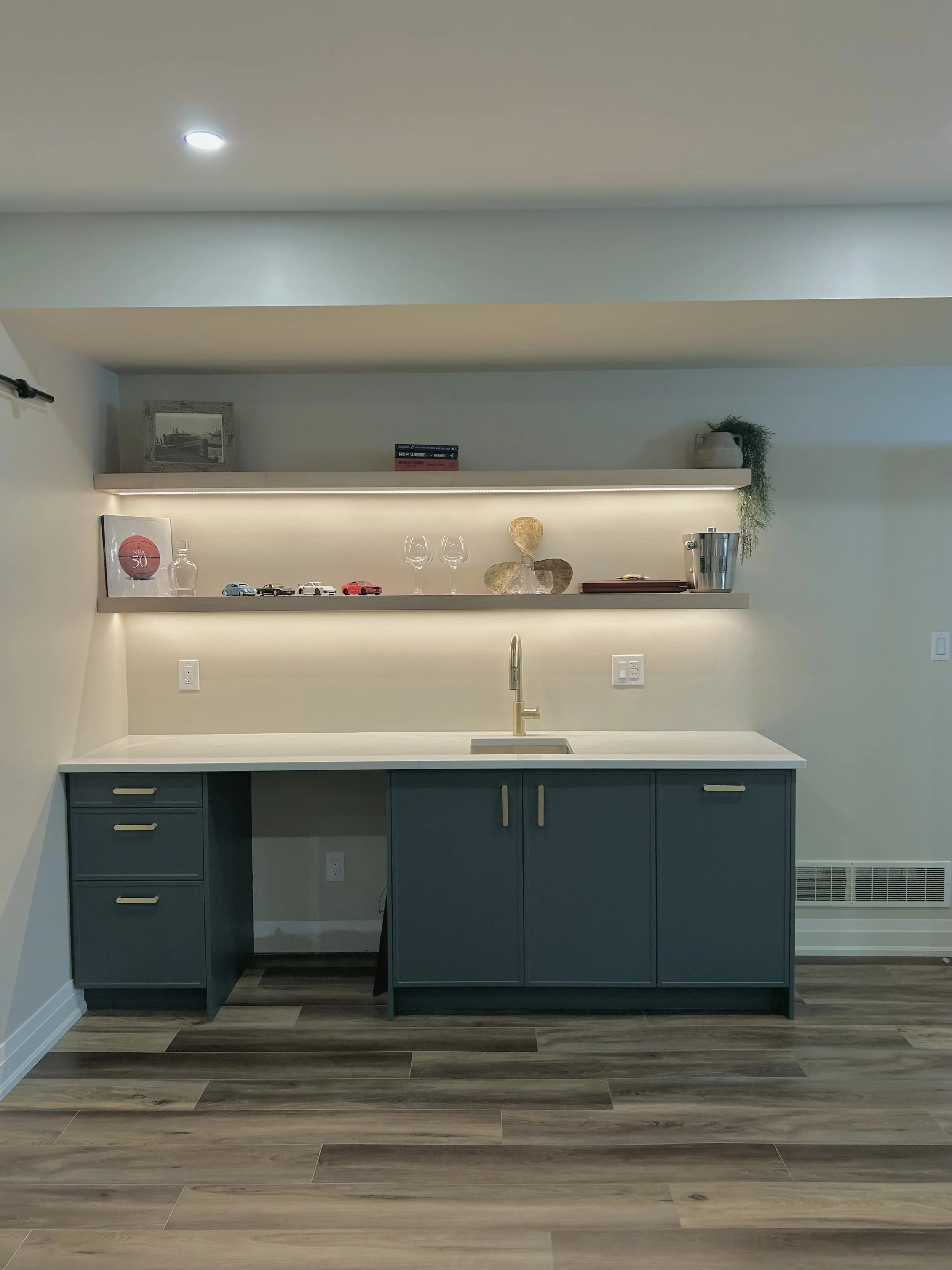 Modern kitchen with blue cabinetry, white countertops, LED light open shelves with decor, a sink with a faucet, and wood-look flooring.