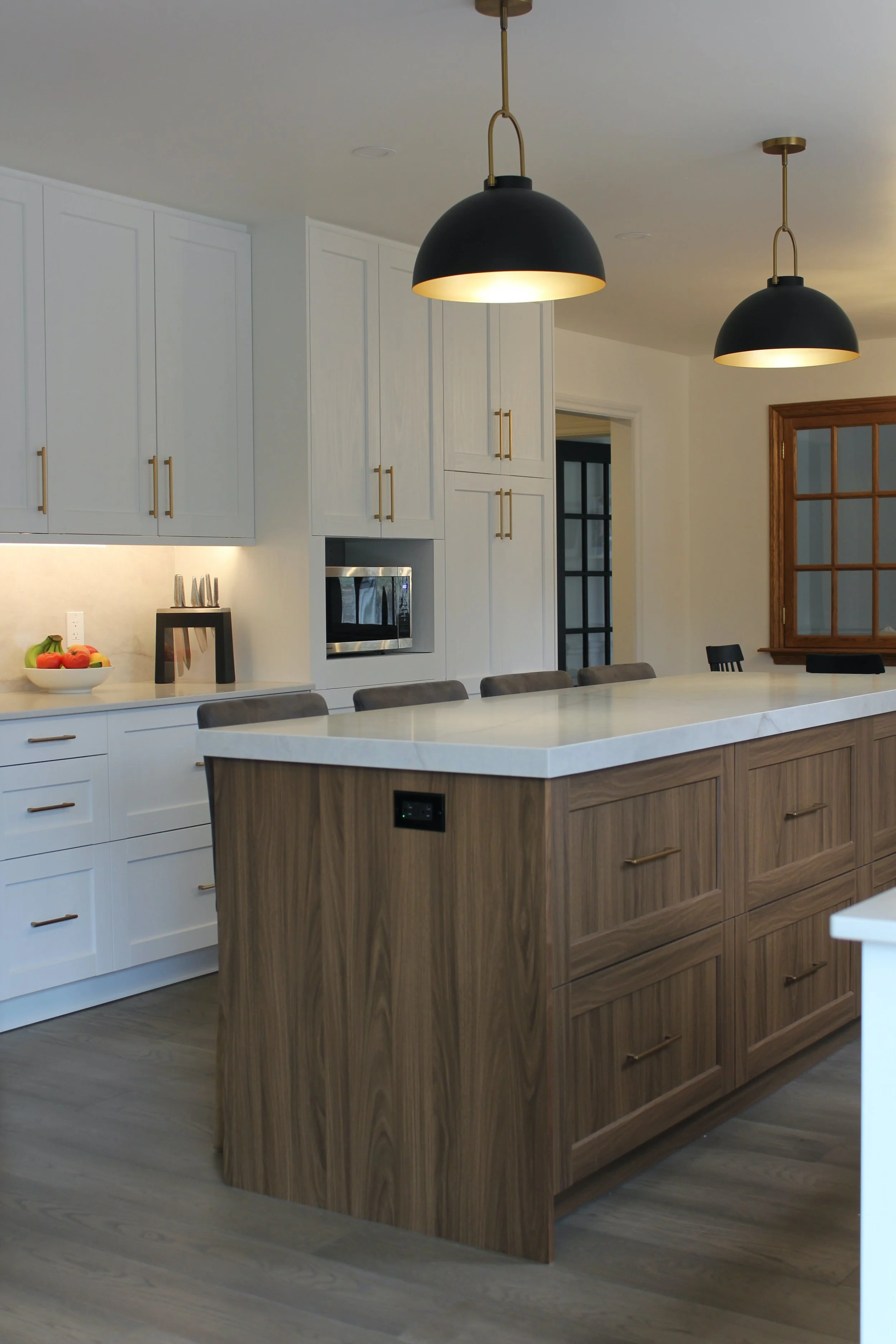 Modern kitchen with white cabinets, two hanging black pendant lights, a wooden island, stainless steel microwave, and a window with wooden trim.