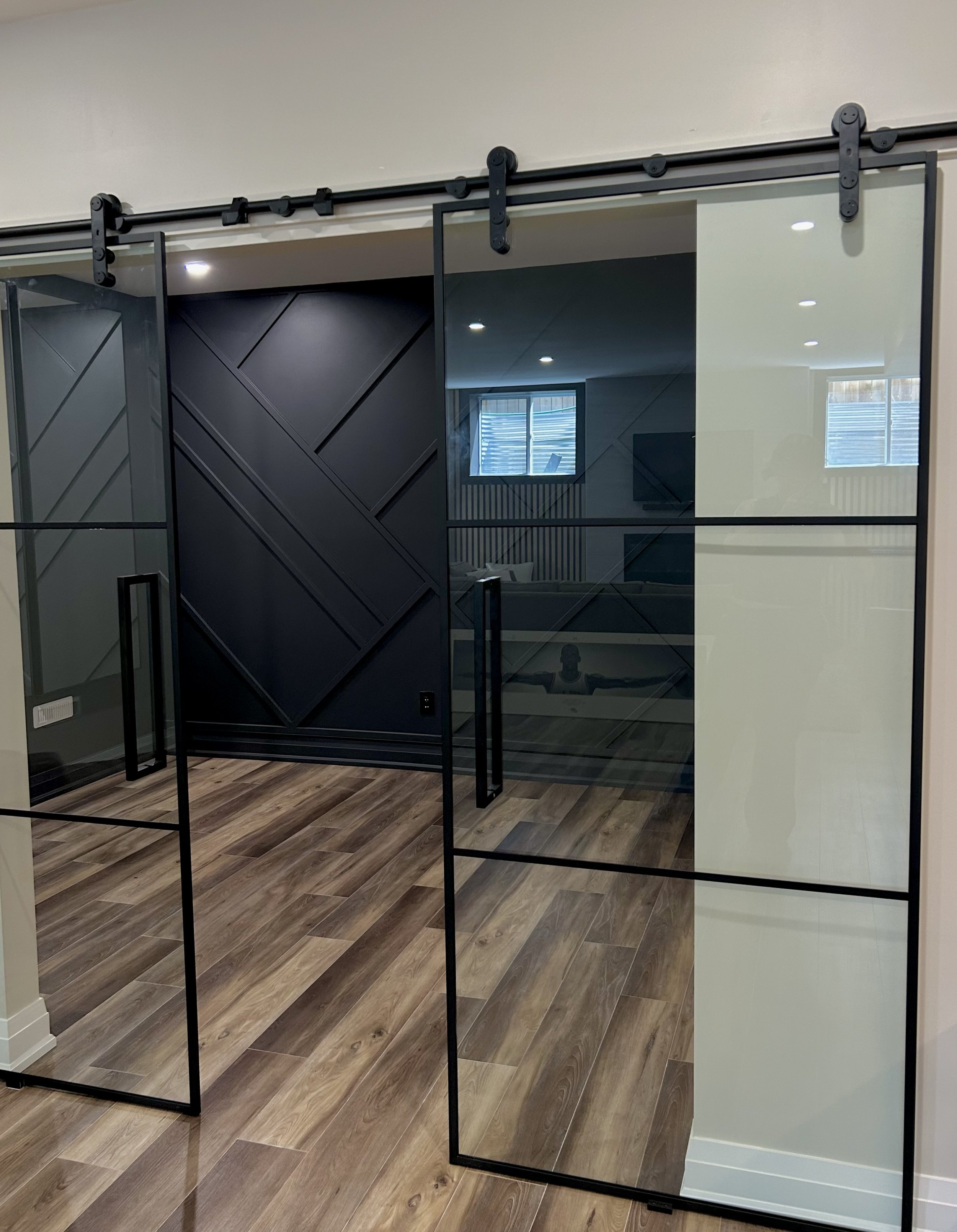 A room with a glass sliding door and wooden floors, with reflections showing a window and some furniture.