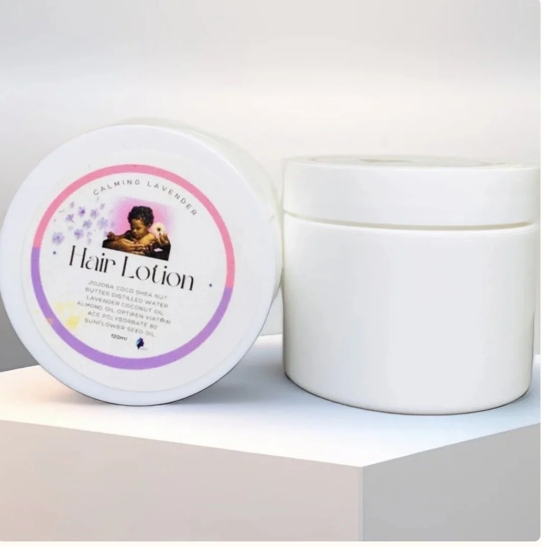 A white container labeled 'Hair Lotion' with a colorful label featuring a child, lavender flowers, and text describing its ingredients, next to an empty white jar, on a white surface.