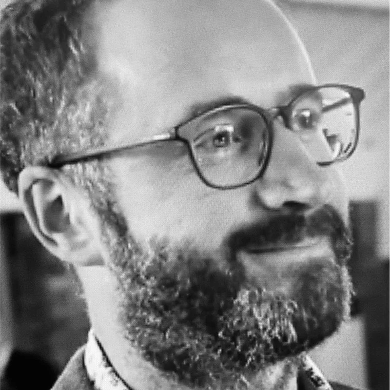 Chris Wilson, Director, wearing glasses and smiling.