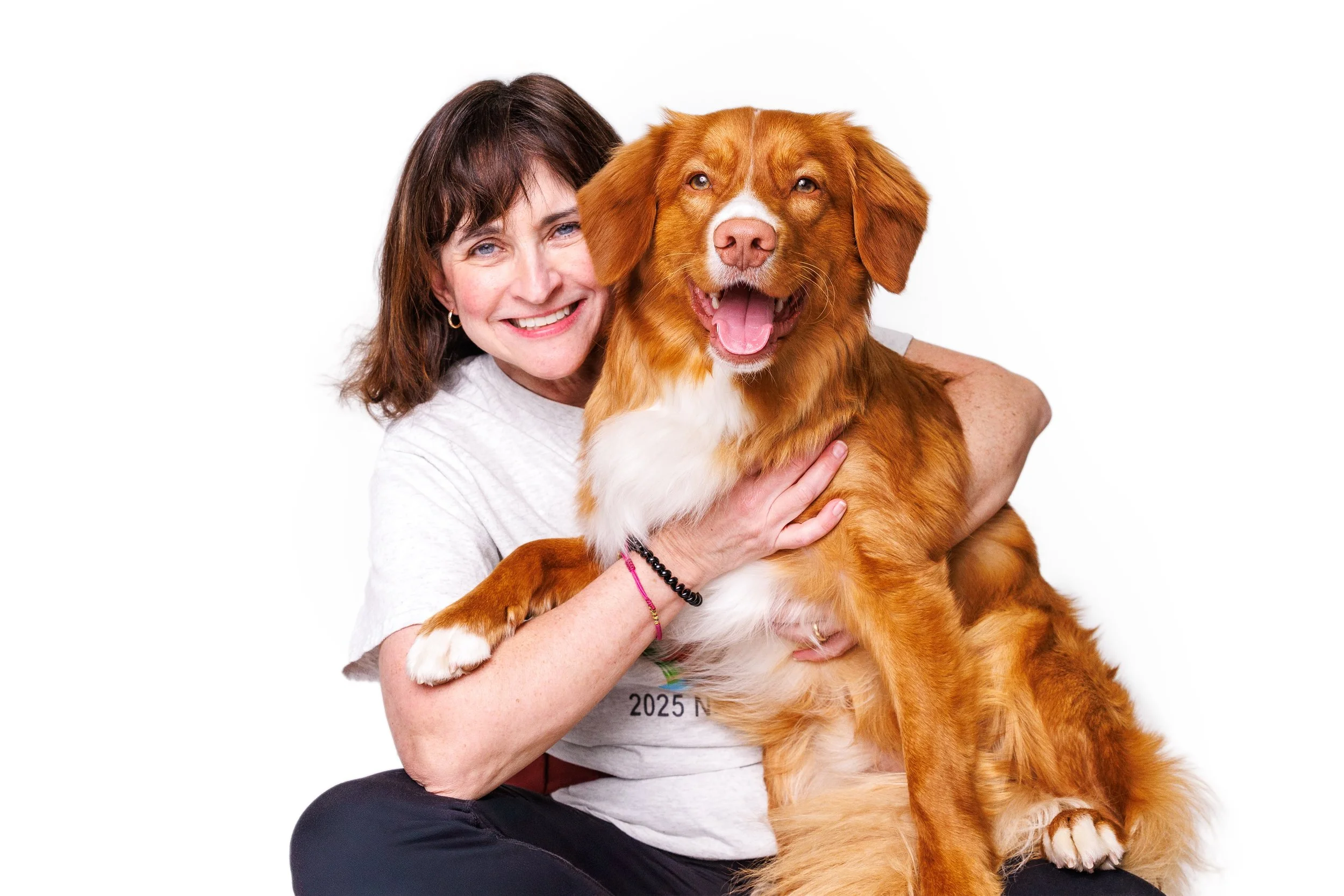 A woman with brown hair and a white shirt smiling and holding a brown and white dog with a happy expression against a white background. Raleigh Pet Photography. 