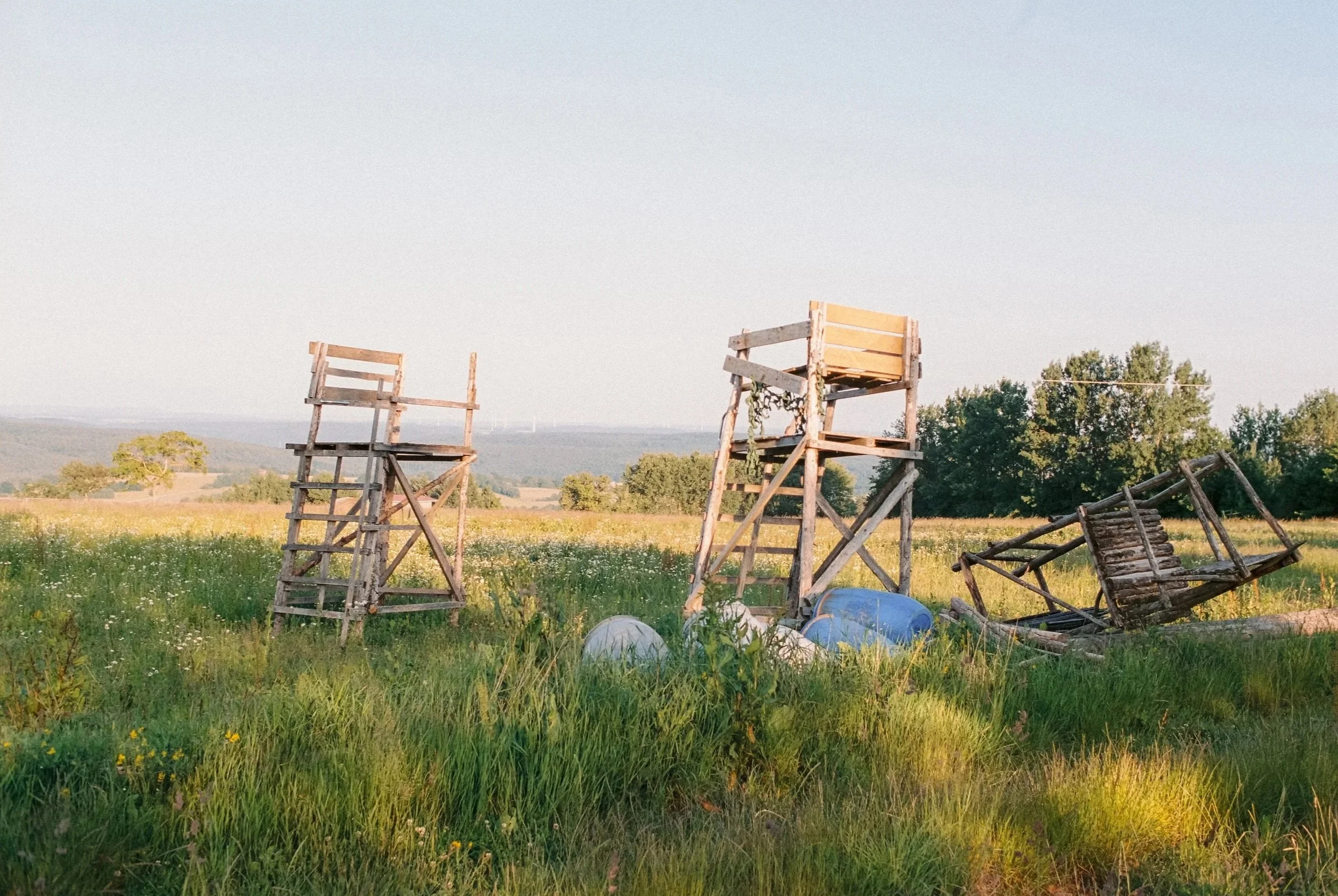Verfallsene Holzaufstiege und eine umgestürzte Holztruhe in einem grünen Feld bei Sonnenuntergang. Fotografiert auf Portra 400.