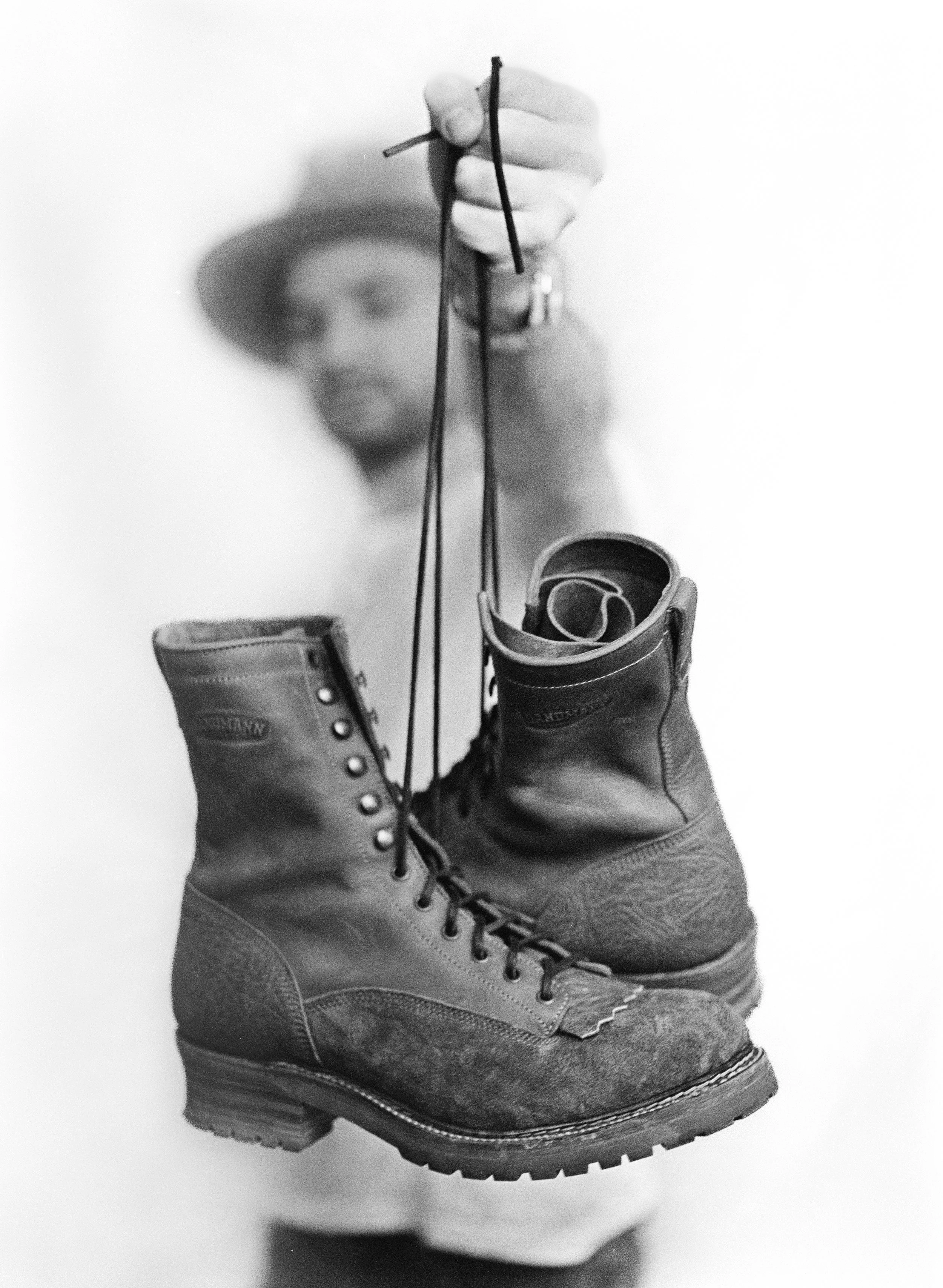 Model in weißem T-shirt hält zwei Boots von dem Schuhhersteller Sandmancraft. Analog Ilfold HP5 Film geschossen mit Mamiya 645.