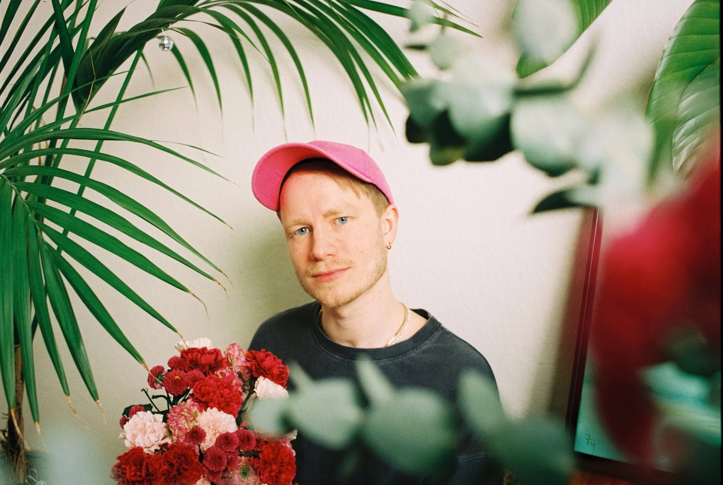 Björn Amadeus mit pinker Cap, umgeben von grünen Pflanzen und roten Blumen