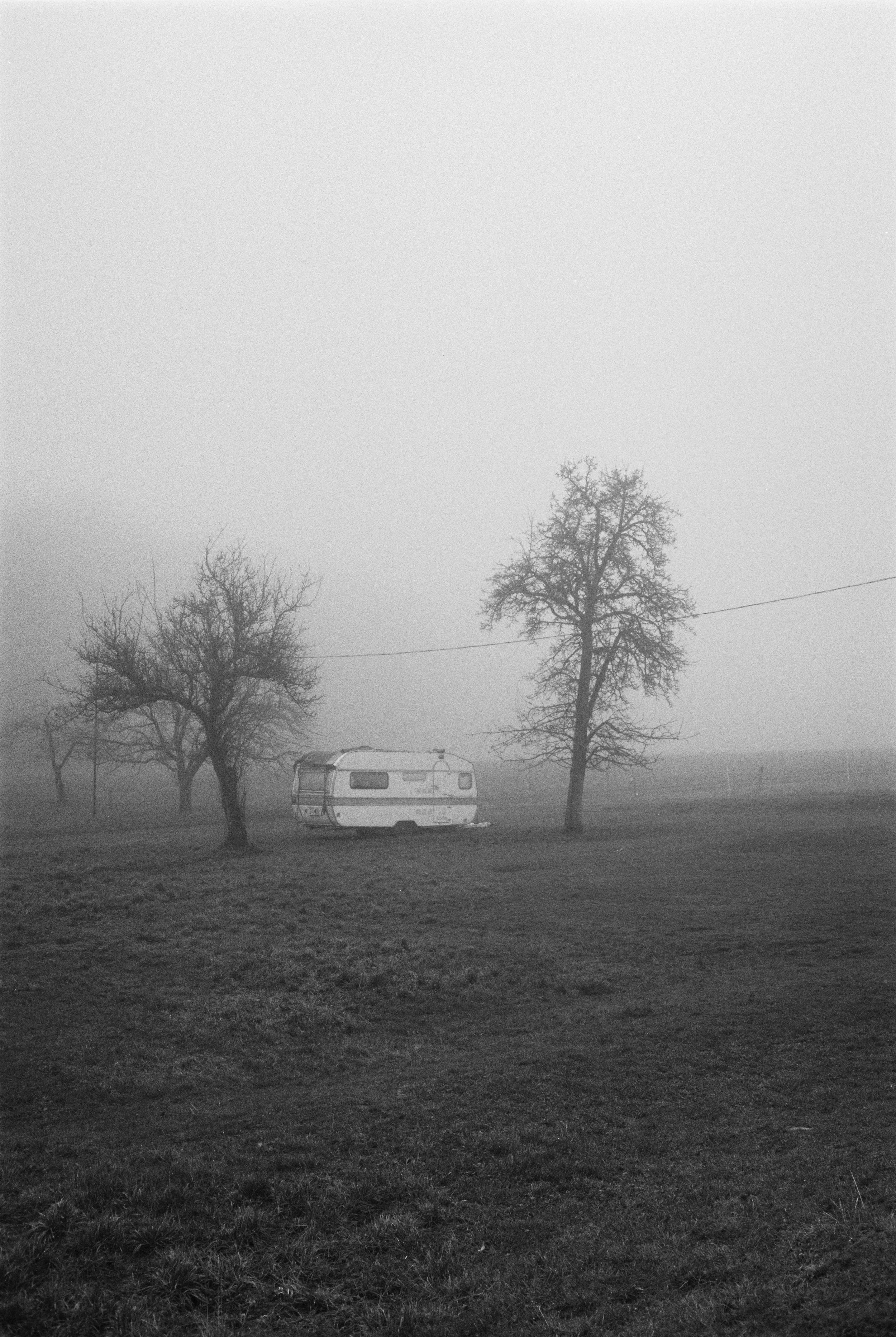 Ein Zelt oder Wohnwagen in einer nebligen, kargen Landschaft mit zwei kahlen Bäumen auf der Wiese. Langenleiten auf Film.