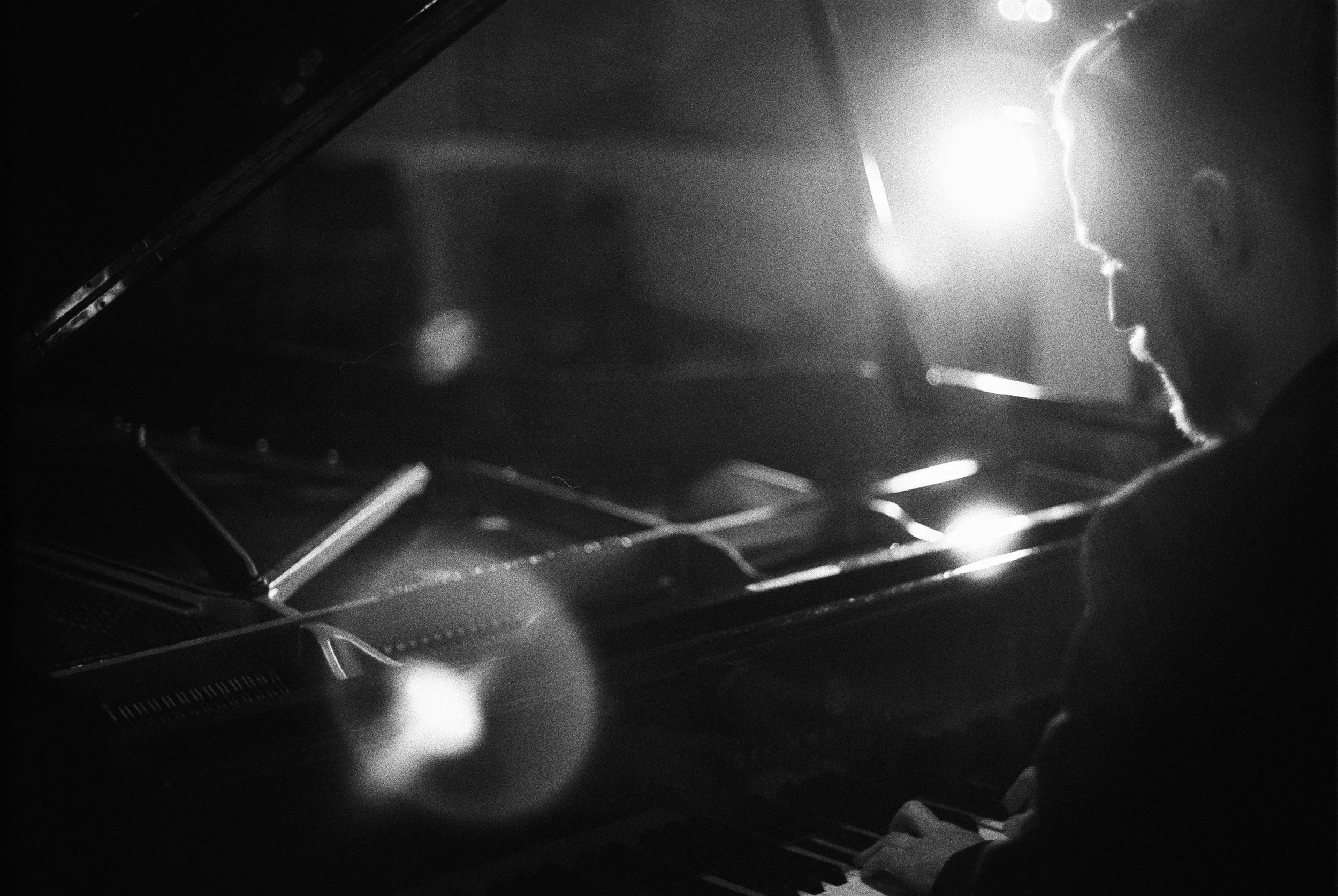 Schwarz-weiß-Foto eines Mannes, der auf einem Flügel Klavier spielt, mit Lichtstrahlen im Hintergrund.