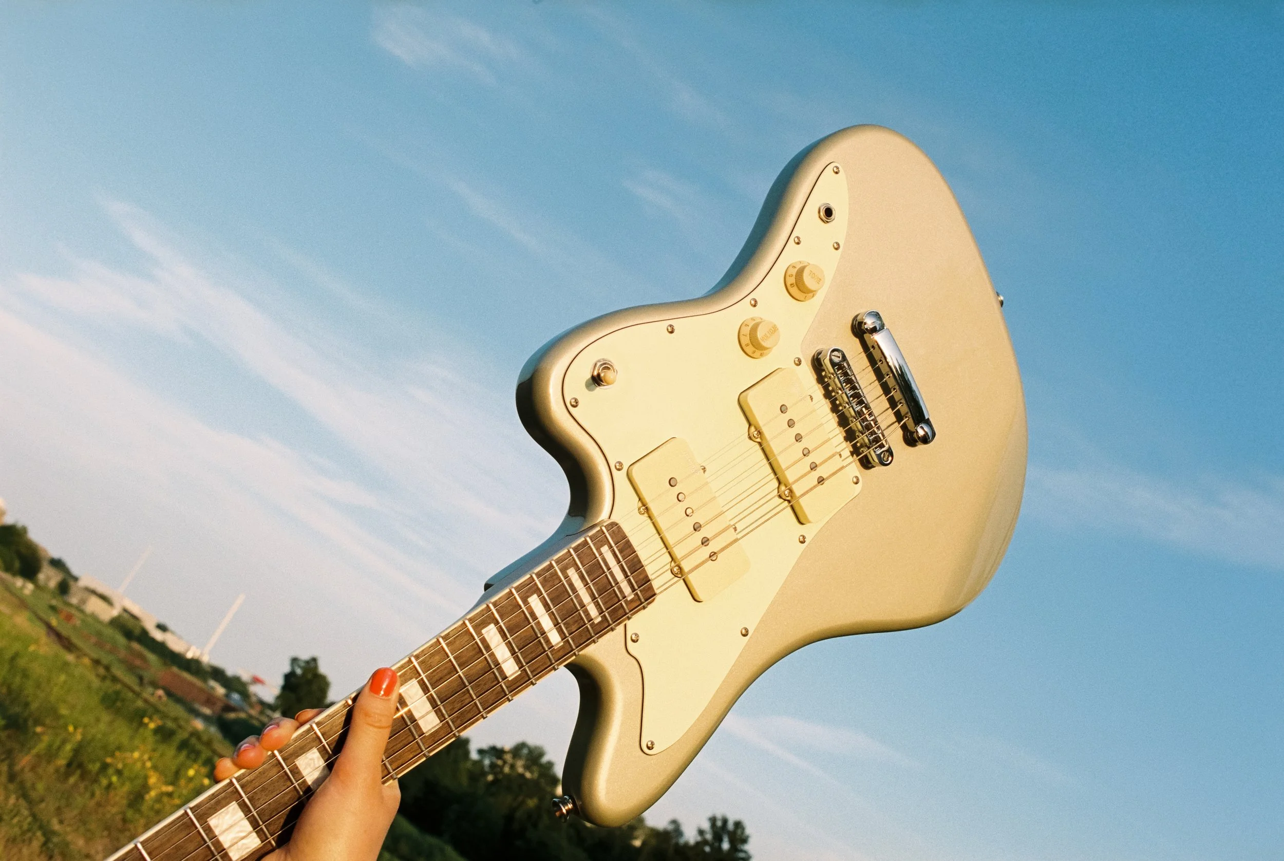 Ein Harley Benton JA-60 E-Guitar in Cremetöne wird gegen den Himmel gehalten. Geschossen auf Portra 400 mit der Nikon F2.