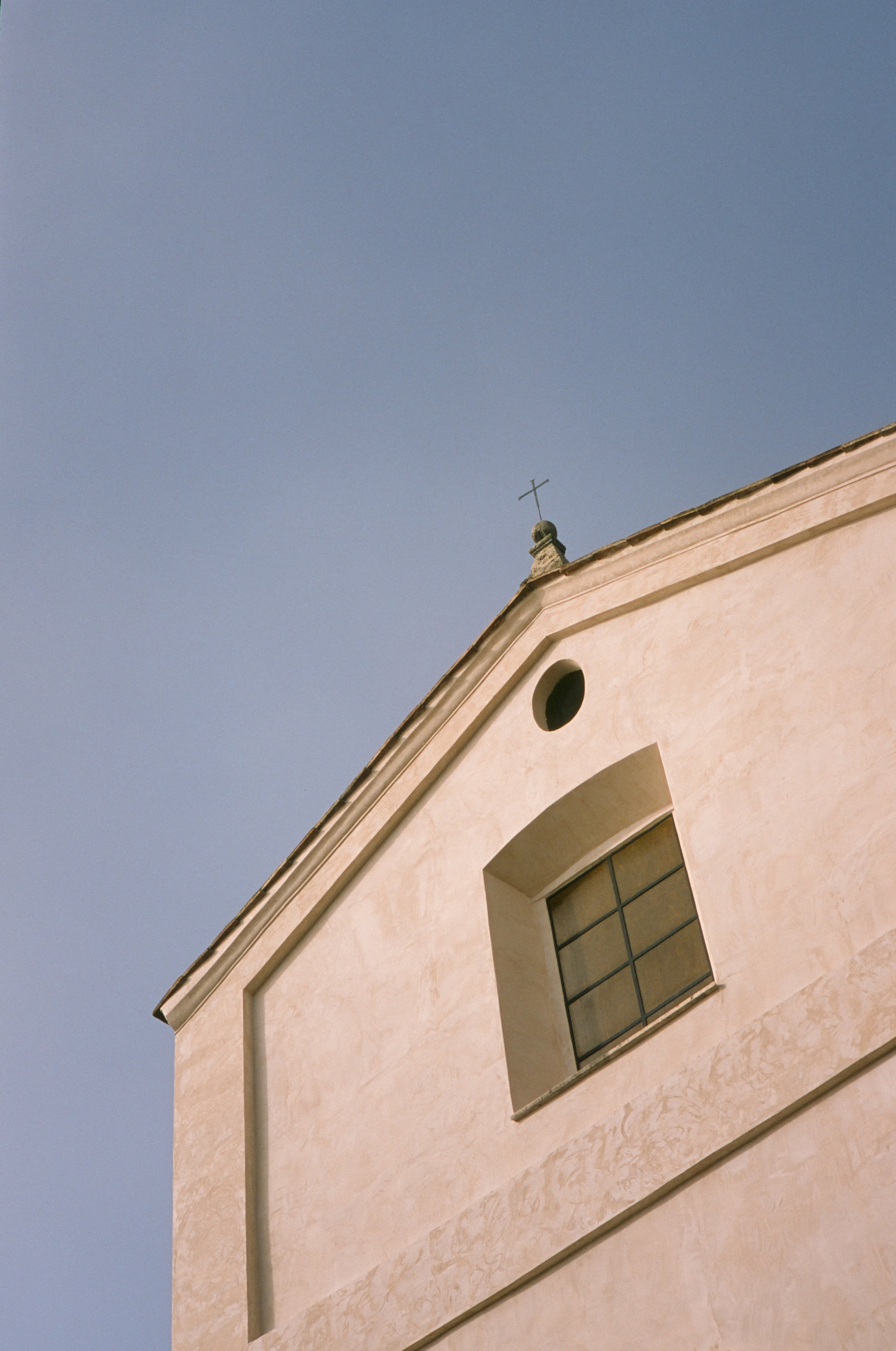 Aufsicht auf einen hellen Kirchturm mit Kreuz auf dem Dach und einem großen Fenster, gegen einen blauen Himmel. Orte VT auf Ektachrome.