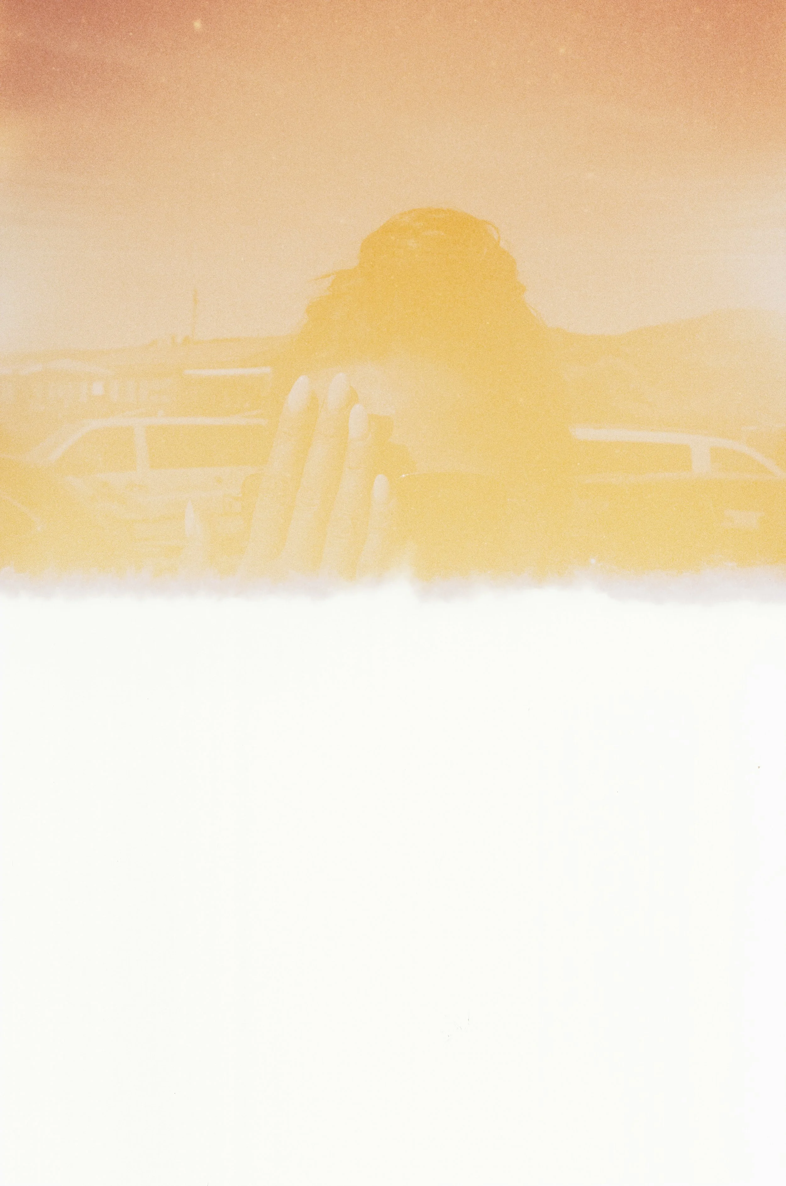 Ein Mädchen hält eine Kamera vor ihr Gesicht, während sie nach draußen blickt, im Hintergrund sind Fahrzeuge zu sehen, die Szene ist in einem warmen Gelbton gehalten. Fotografiert auf abgelaufenem Diafilm.