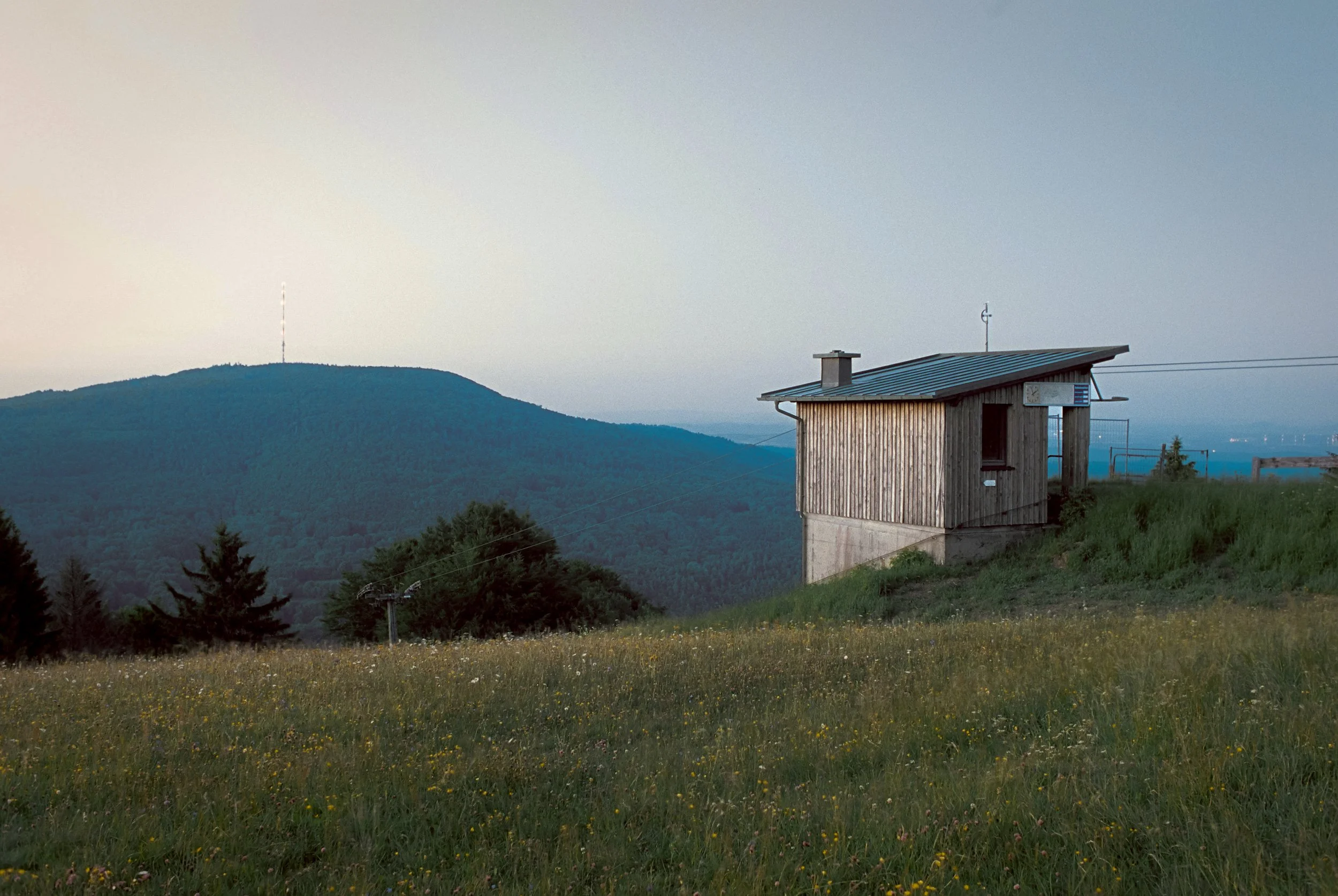 Kleines Holzhaus auf einer grünen Wiese mit Hügeln im Hintergrund bei Sonnenuntergang. Geschossen auf Portra 400.