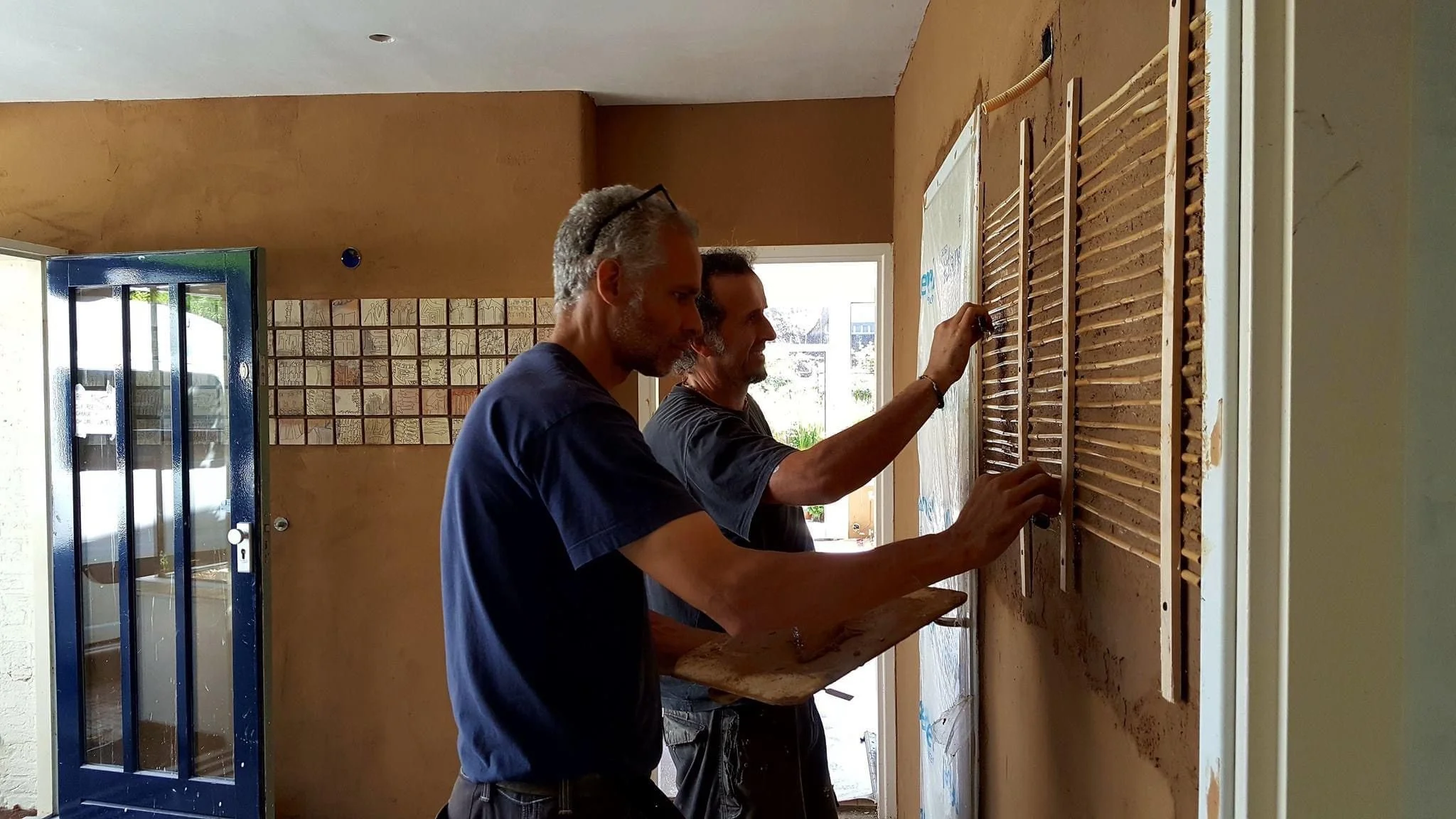 The Best Plasterers With Clay at Work Two men are covering a wall heater on the wall in a house with clay plaster.