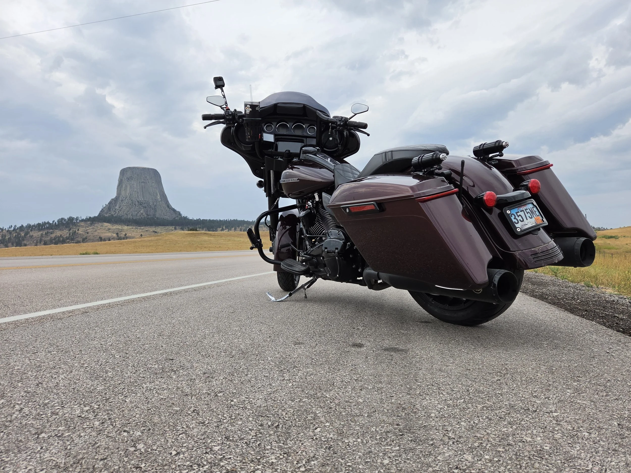 A maroon and black touring motorcycle parked on the side of a highway with a scenic landscape background including a large butte and cloudy sky.