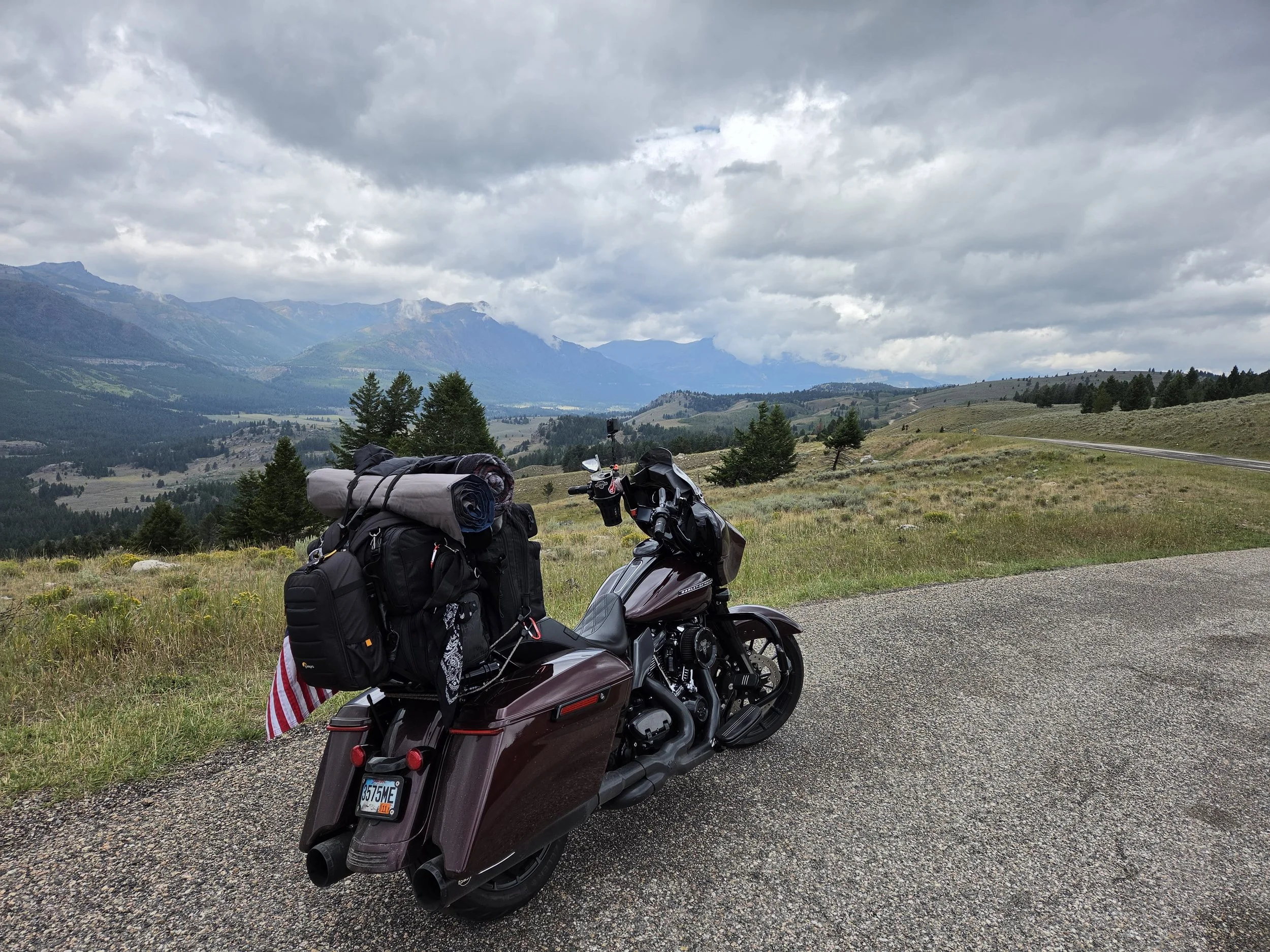Motorcycle parked on a gravel road in a scenic mountainous area with cloudy sky, carrying luggage and gear.