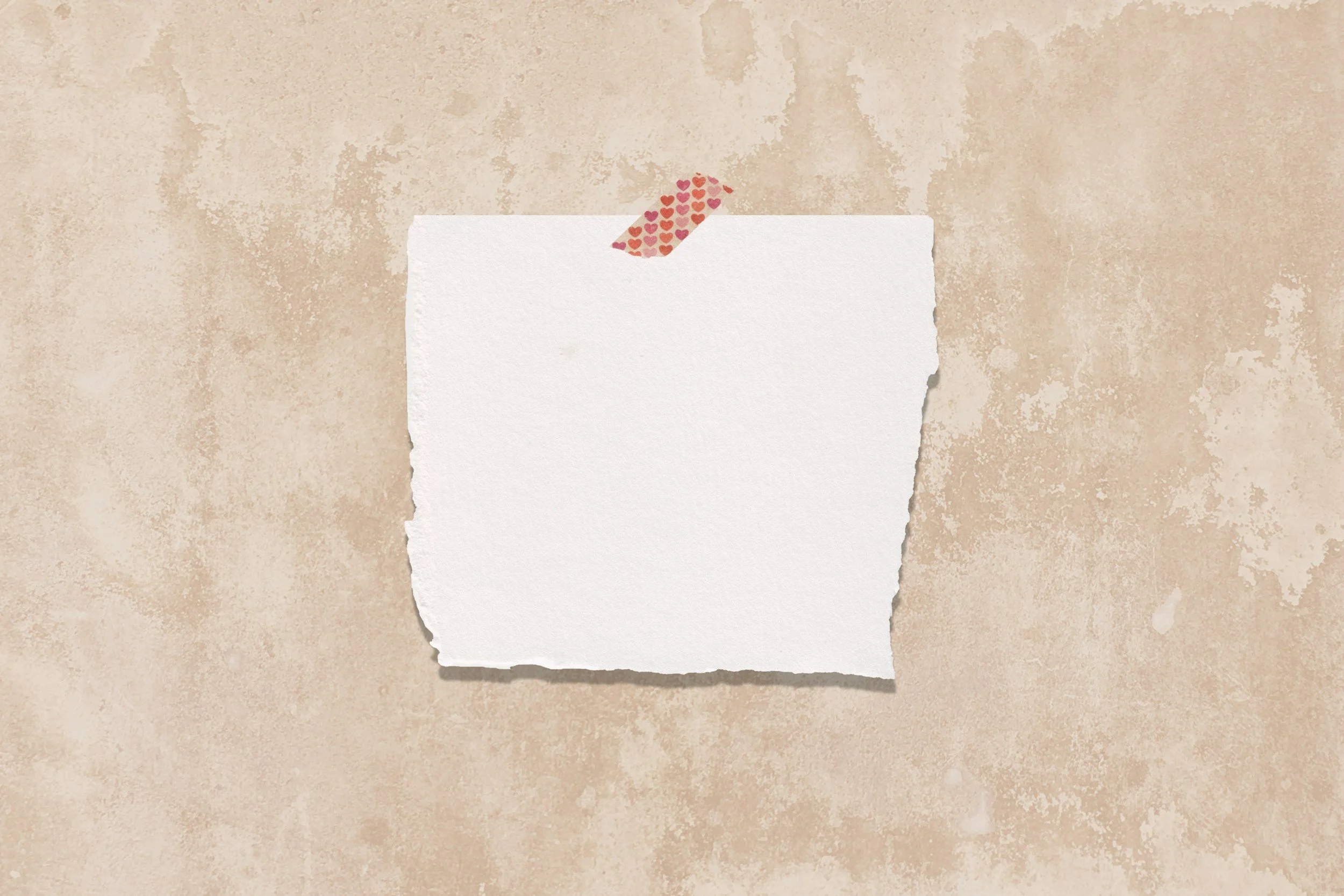 A blank white piece of paper with torn edges, taped to a textured beige wall with a small strip of decorative pink heart-patterned washi tape at the top.
