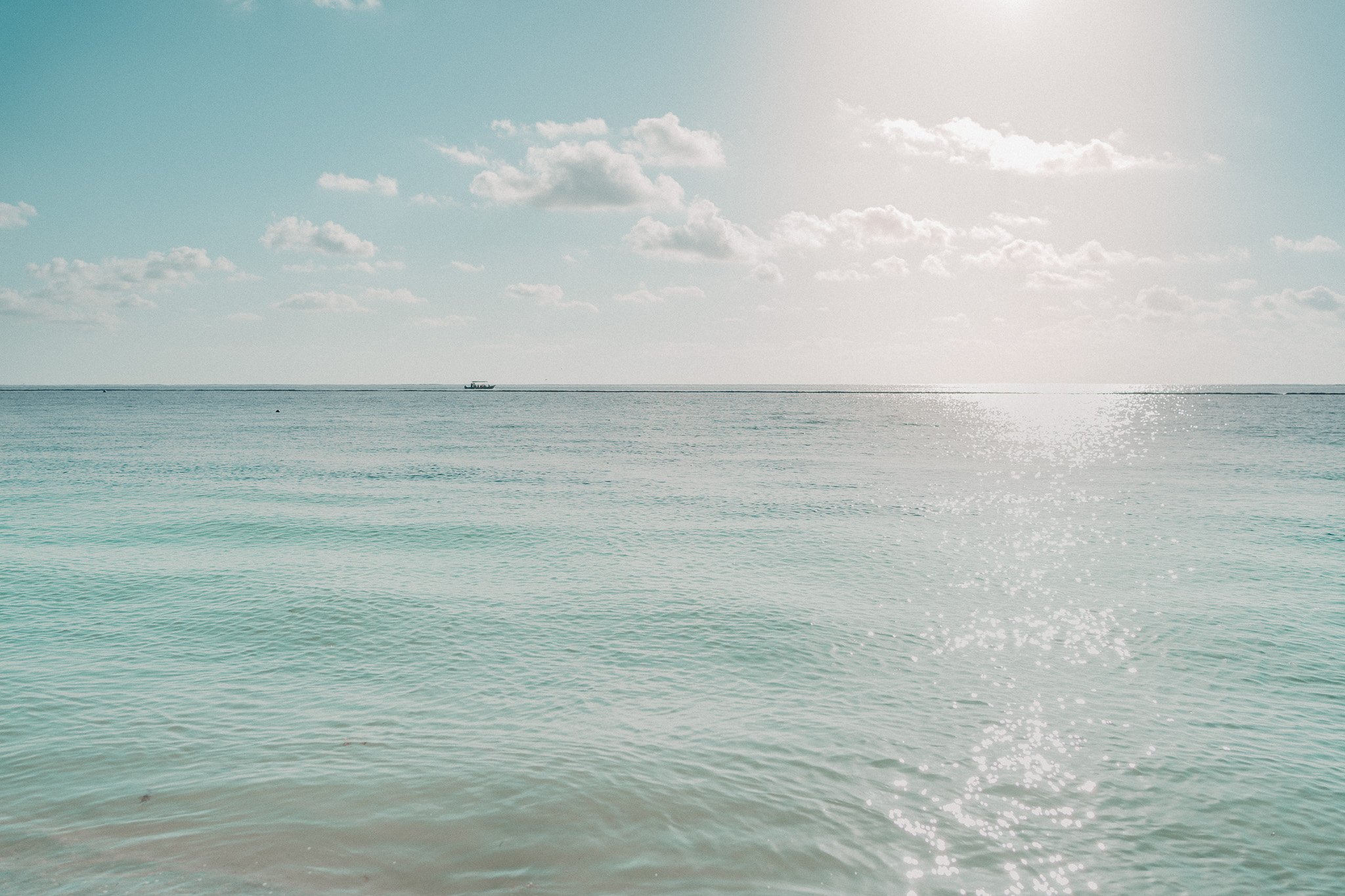 Calm ocean with gentle waves and a boat on the horizon under a partly cloudy sky