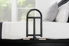 Black metal luggage rack in front of a bed with white bedding and pillows, near a window.