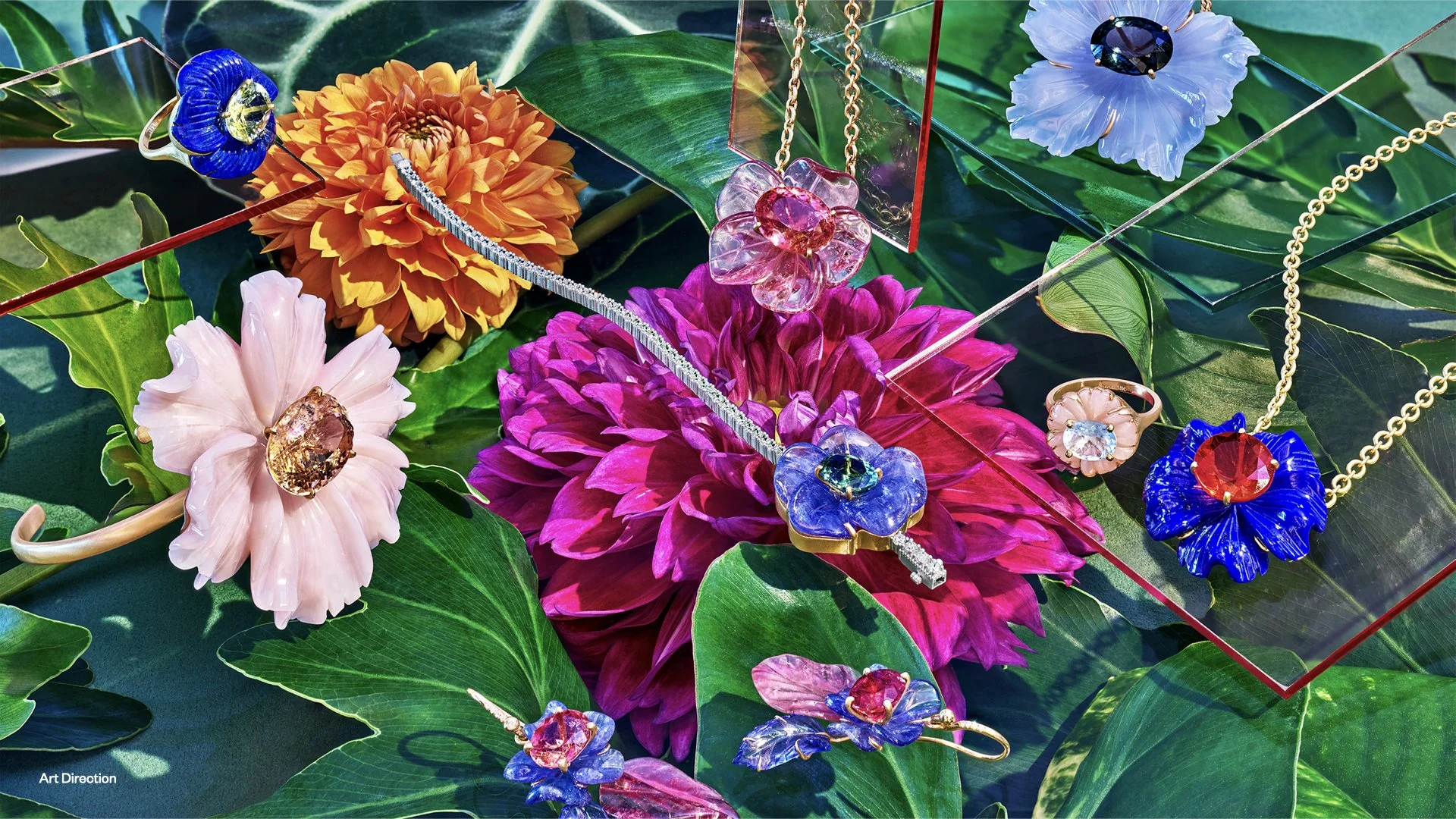 Jewelry display with colorful flower-shaped necklaces, rings, and earrings on a bed of green leaves and vibrant flowers.