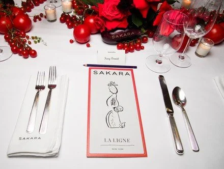 Table setting at Sakara restaurant with napkins, silverware, wine glasses, a menu, and holiday decorations.