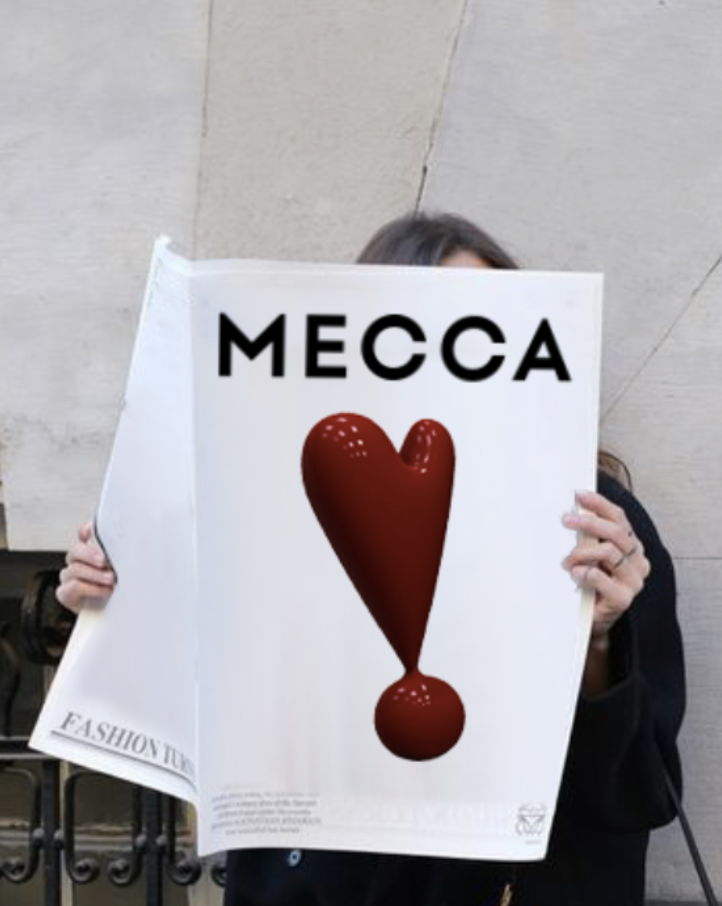 Person holding a sign that says 'MECCA' with a large red heart and exclamation mark