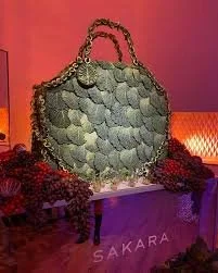 A large handbag with a chain strap displayed on a table at a Sakara event, decorated with purple flowers.
