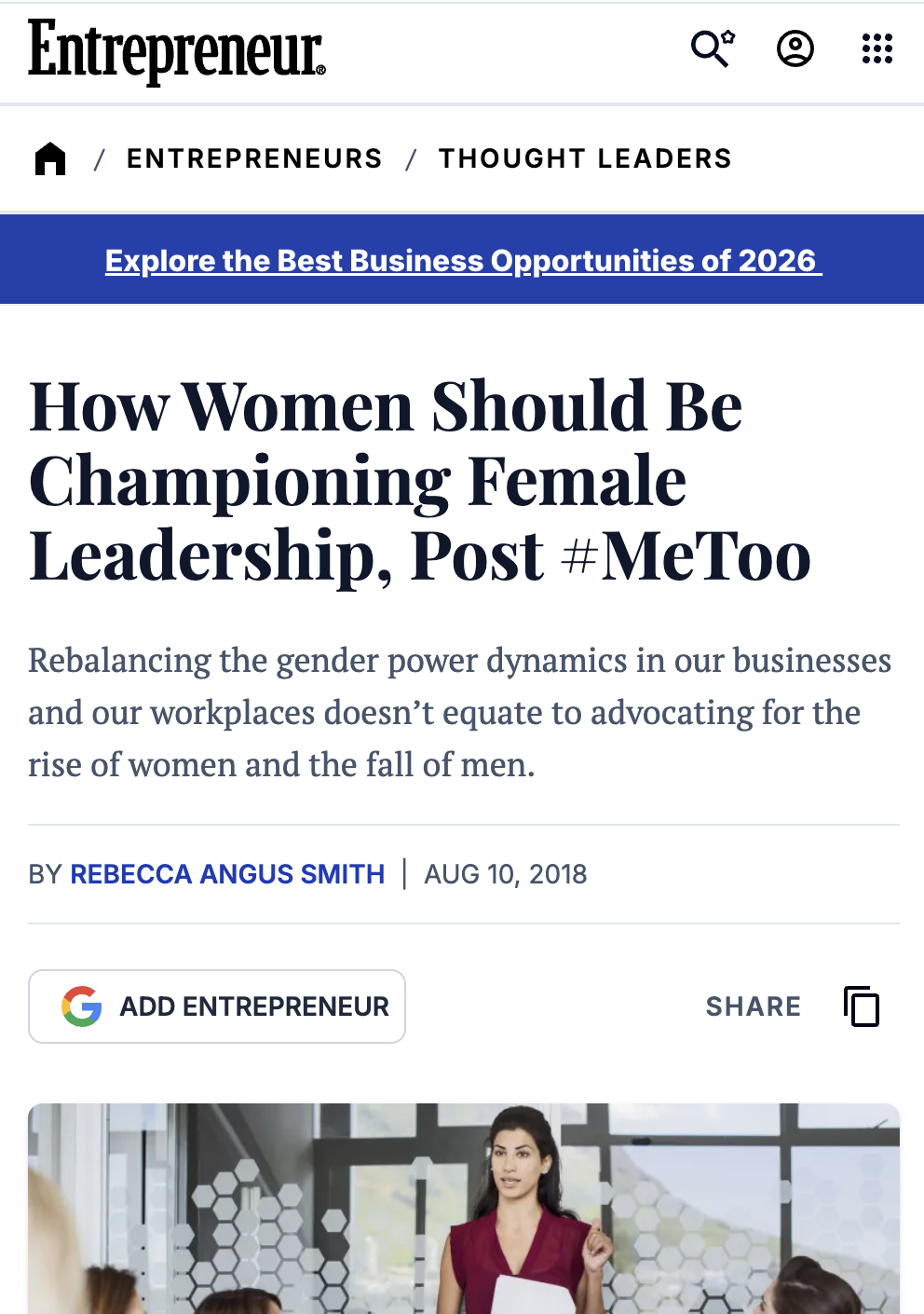 A woman in a red outfit speaking to a group of people in a modern office conference room with large windows.