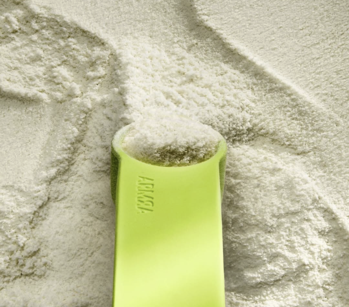 A green plastic scoop filled with white powdery substance, resting on a surface covered with the same white powder.