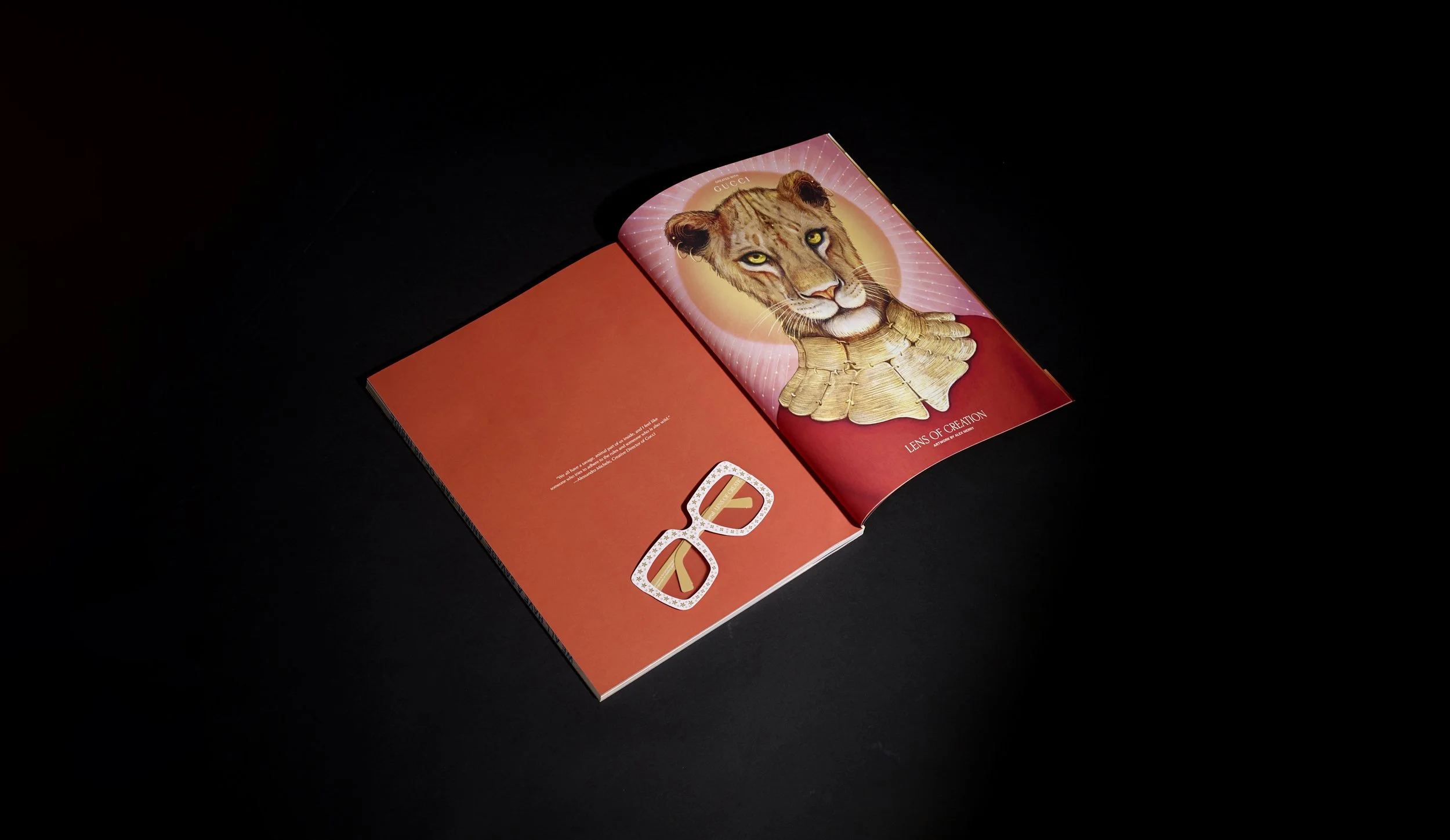 Open book on black background showing a drawing of a lion's head with a circular halo and golden body, with yellow eyes and detailed fur.