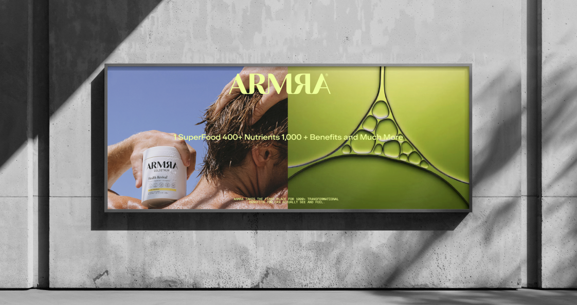 Billboard advertising a health supplement called ARMR. It features a man holding a container of ARMR colostrum on the left side, with a blue sky background, and a green cellular structure illustration on the right side. The text promotes the product'