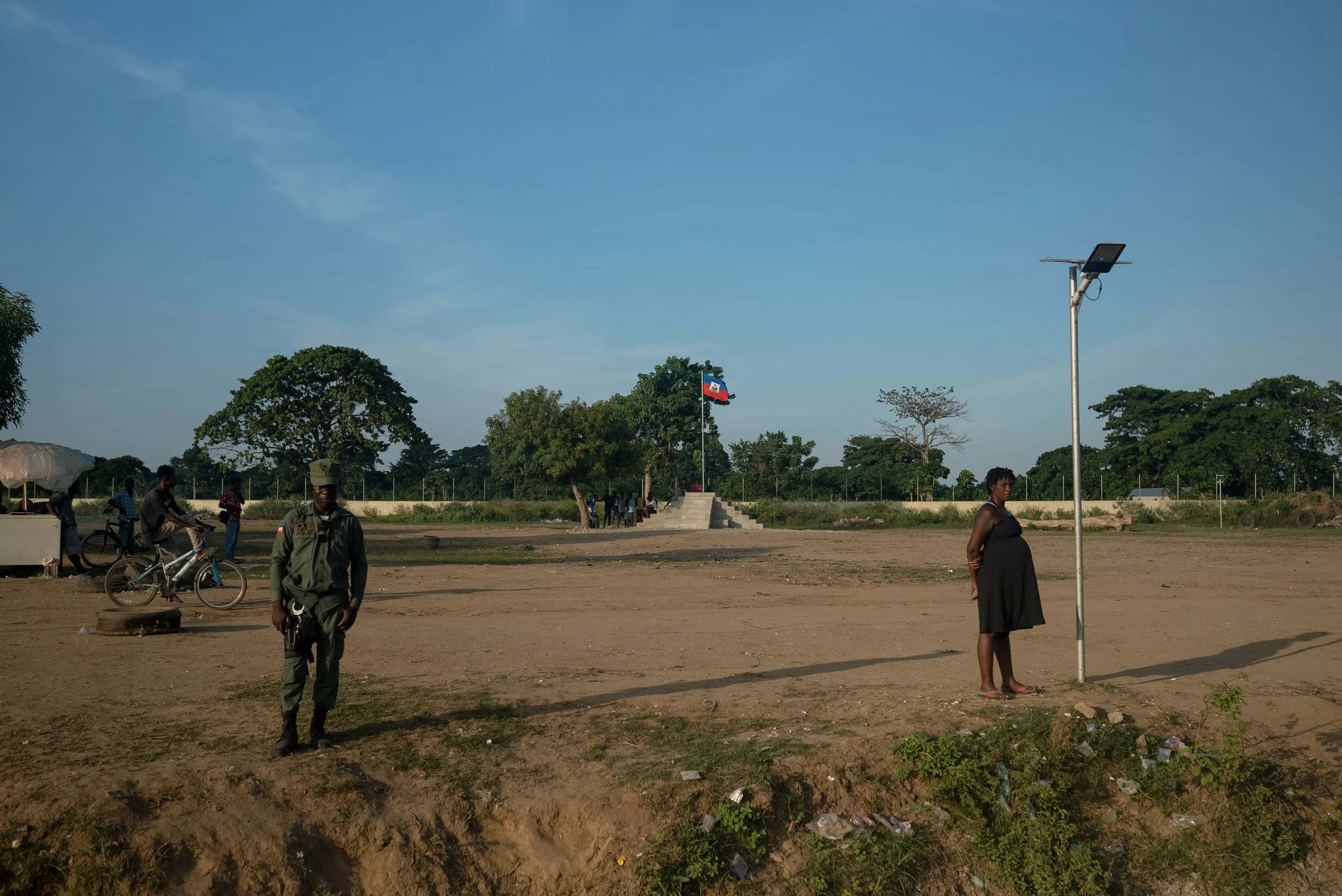 A Haitian Brigade for the Security of Protected Areas (BSAP) Officer stands guard next to a pregnant woman at the border of Haiti and the Dominican Republic. 