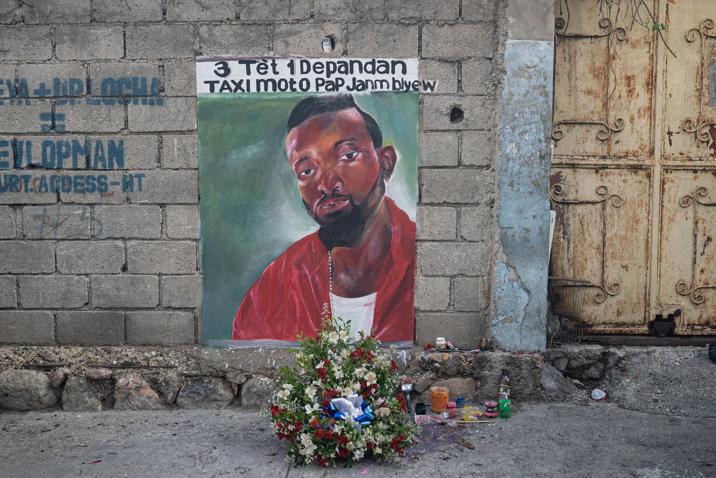 Friends and other motorcycle taxi drivers of the late Johnny Alexis, 33, who was killed by gunfire between gangs and police in downtown Port-au-Prince, hired an artist to paint a mural to commemorate his memory. It reads, "3 heads, 1 dependent. We wi
