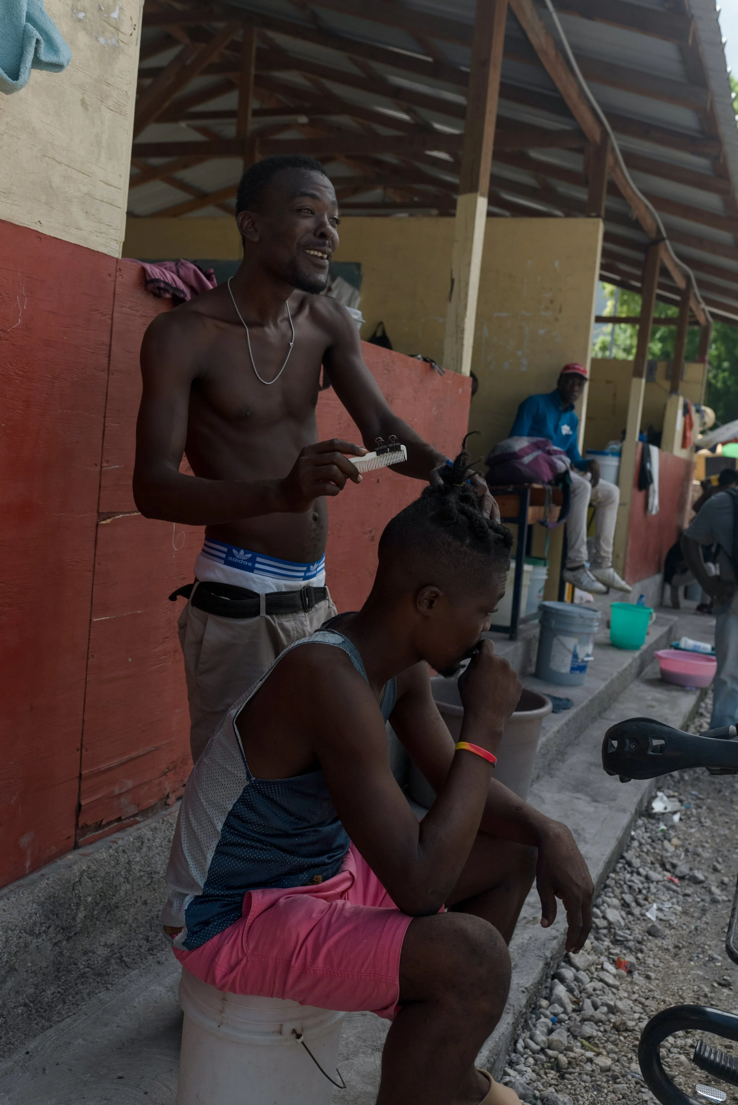 A displaced man cuts a friends hair in the spontaneous camp in a high school in Pacot hosting more than 3,000 refugees from neighboring Carrefour-Feuilles after armed gangs attacked the neighborhood.