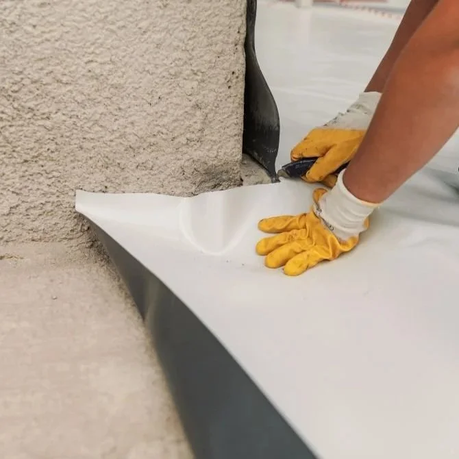 Worker wearing yellow gloves smoothing a white sheet against a textured wall corner