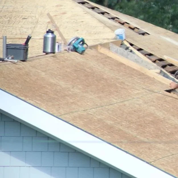 Roof under construction with plywood sheathing, tools, and a worker near the ridge