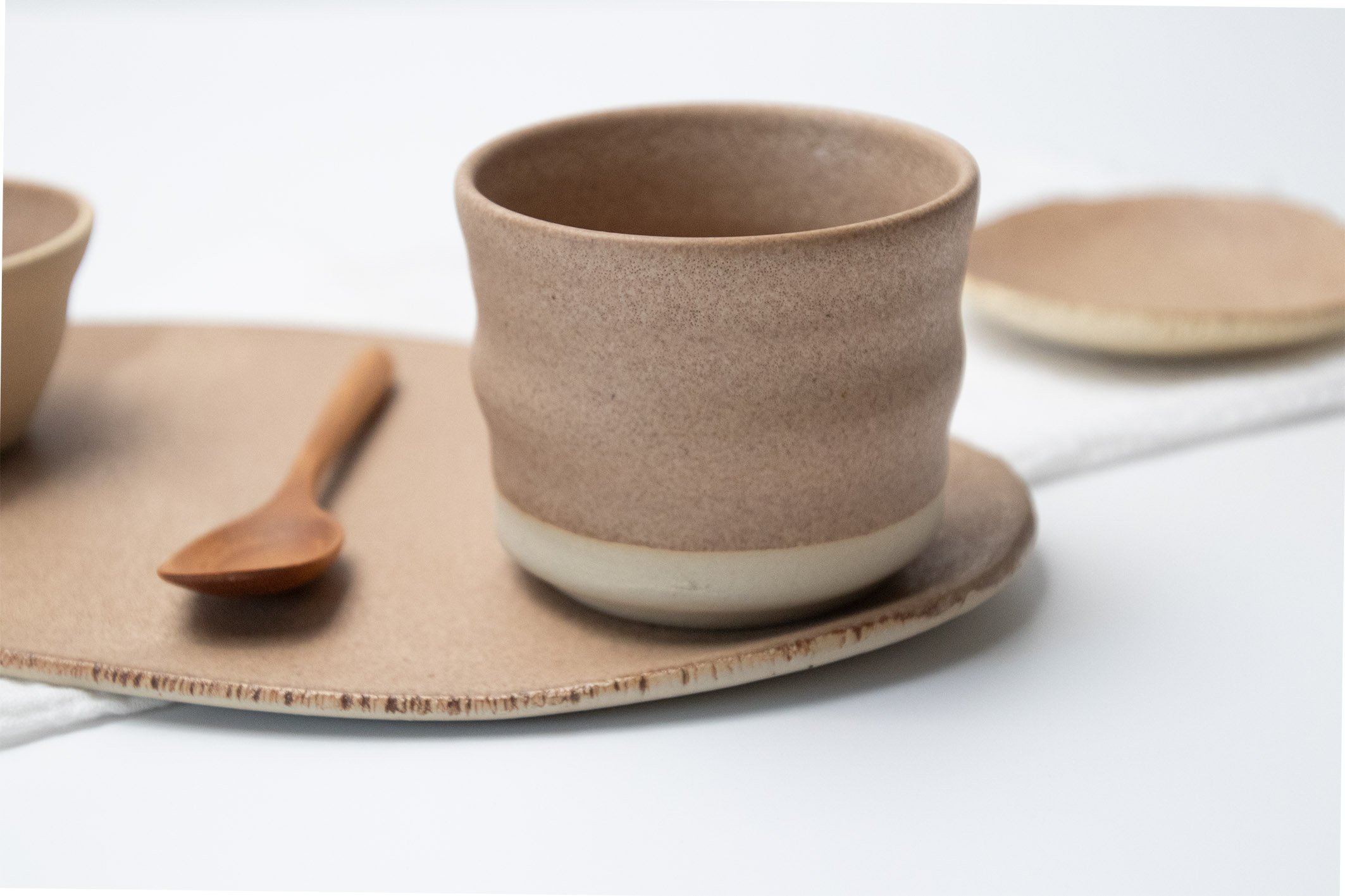 Keramikbecher und Holzlöffel auf einem keramischen Tablett, minimalistisches Design.