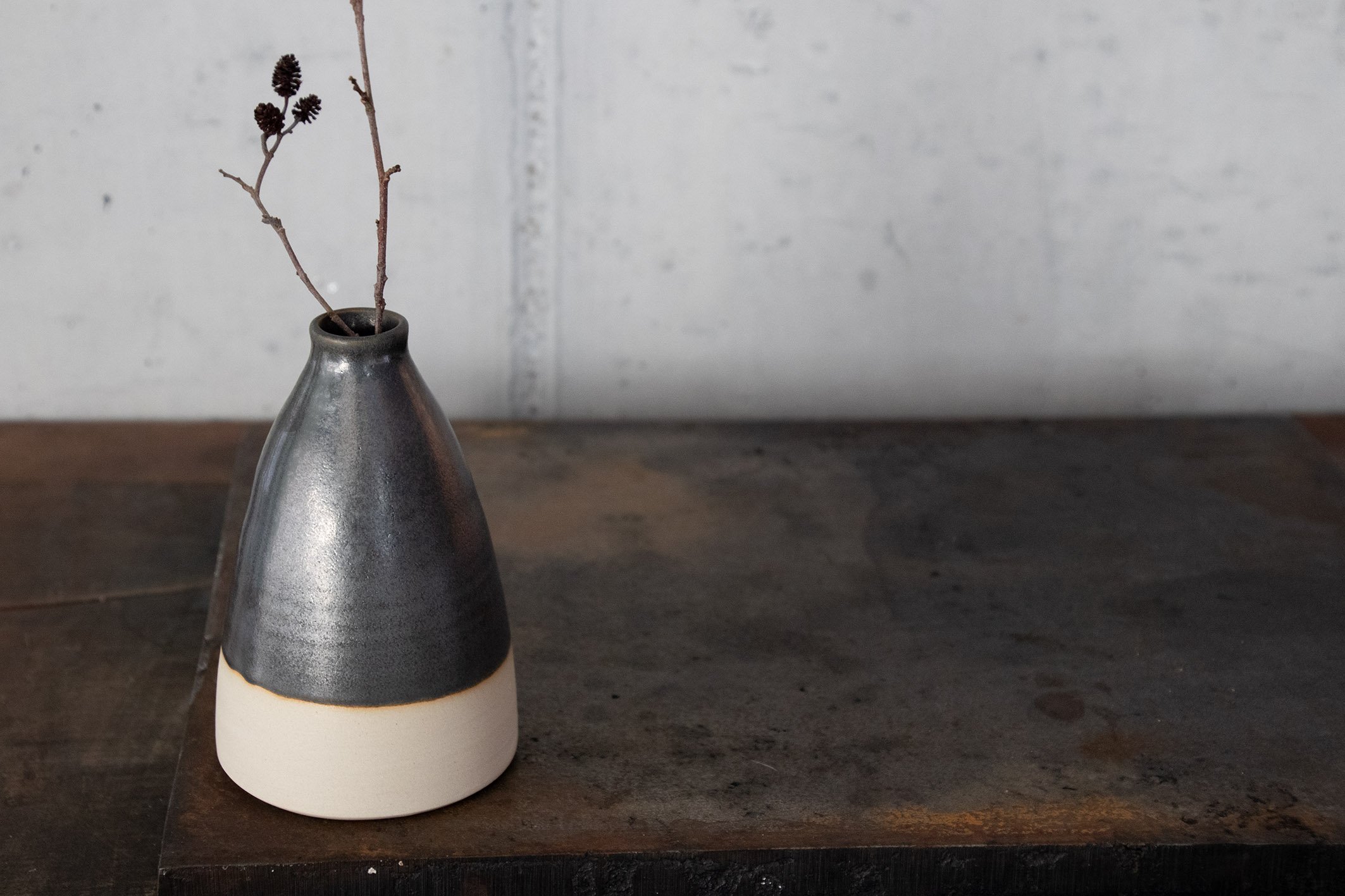 Keramikvase mit Zweigen auf einem Holztisch vor einer weißen Wand.