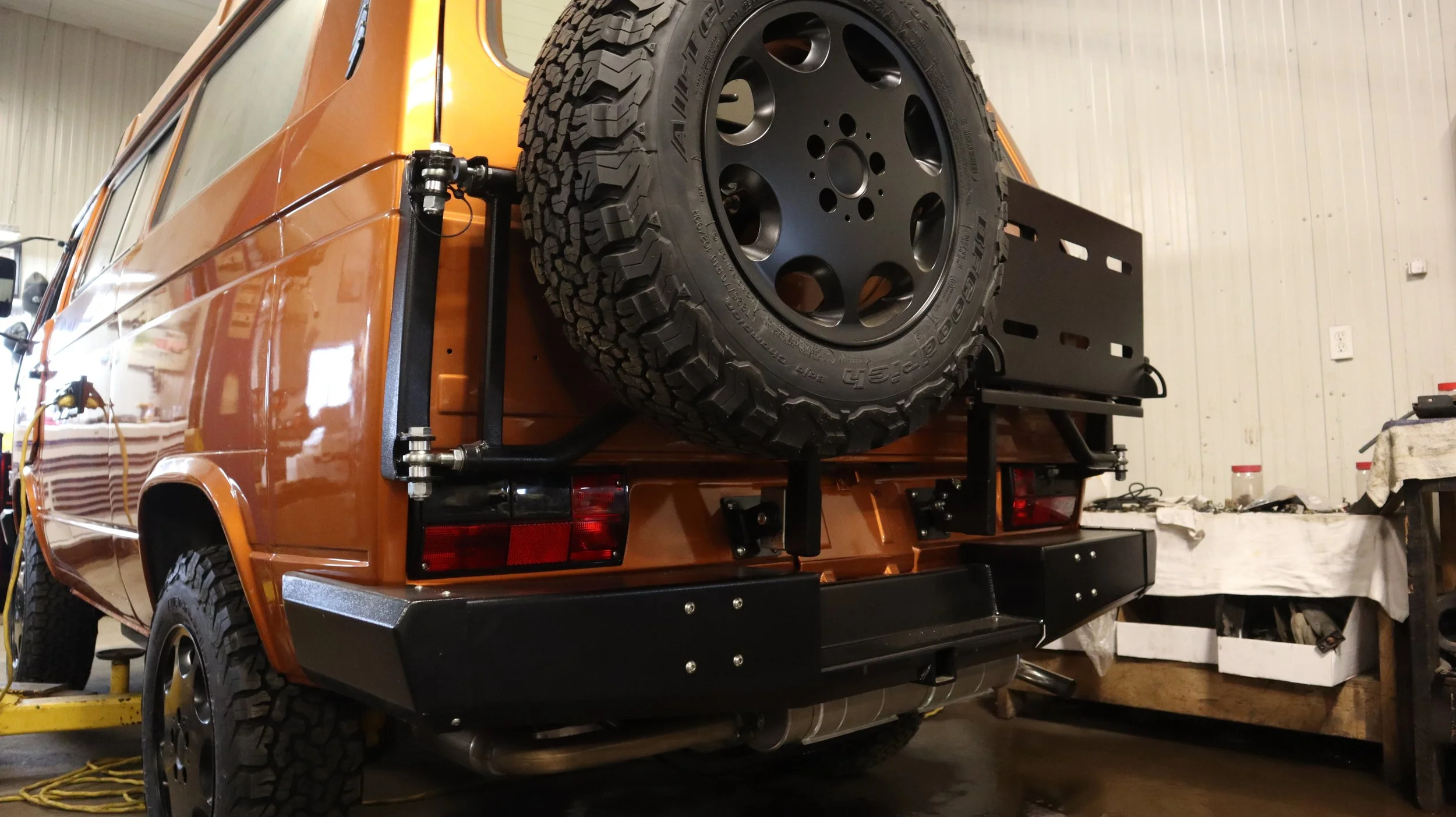 An image depicting a post-installation quality checks inspection on an orange bus with a spare tire on its back.