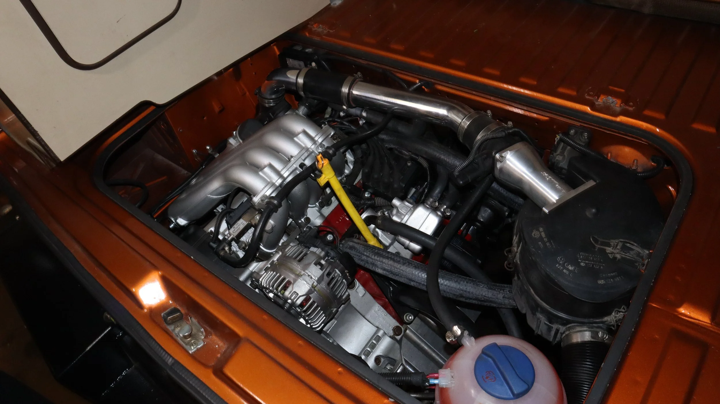 An orange new car engine with attached hose and tubing.