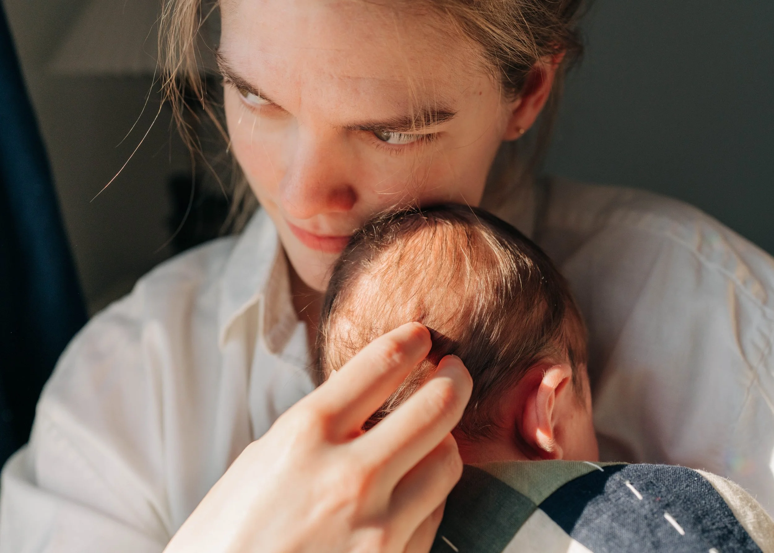 A woman gently cradles and kisses the head of a sleeping baby, showing affection and tenderness.