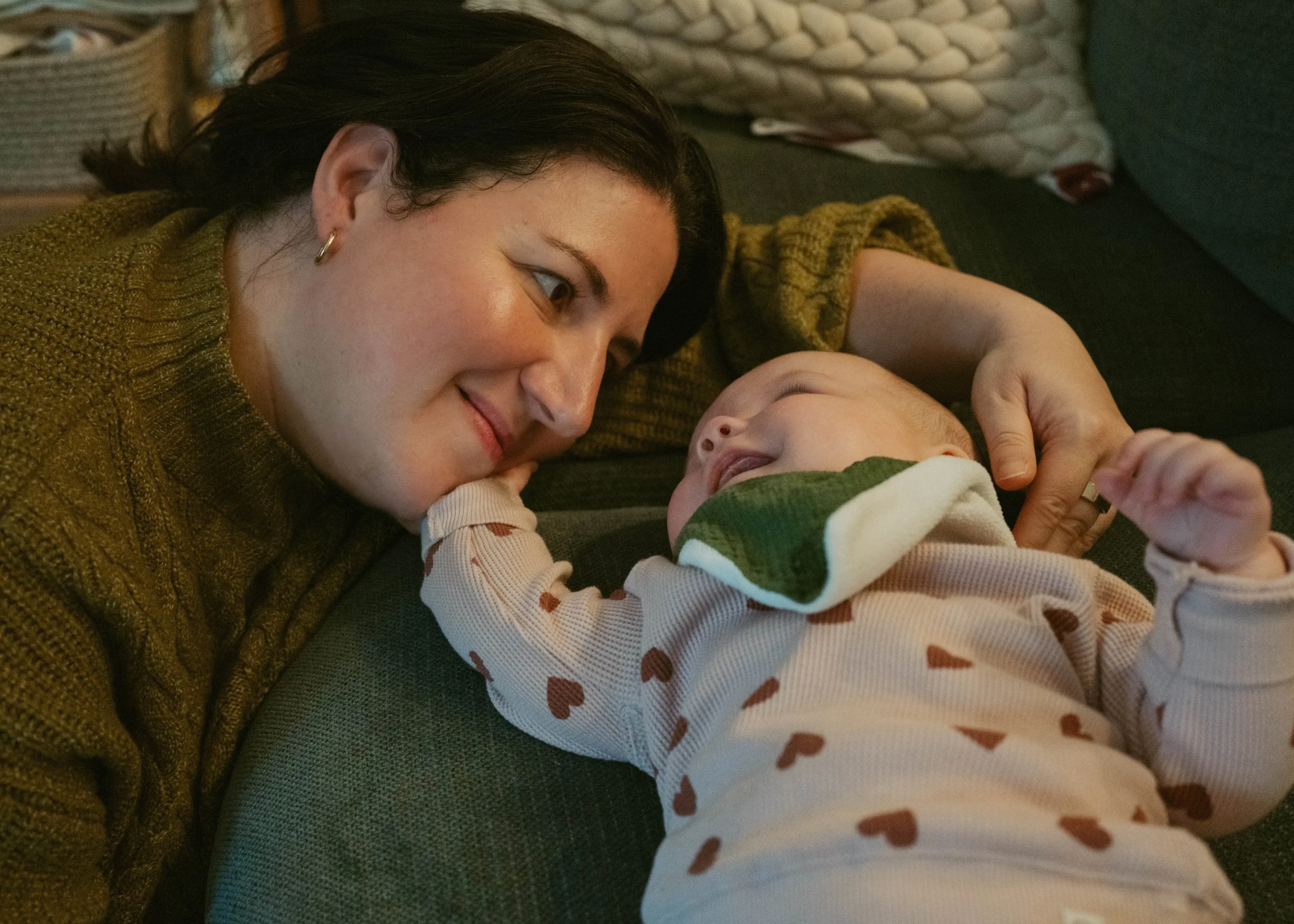 A woman and a baby lying on a couch, gazing at each other and smiling warmly.