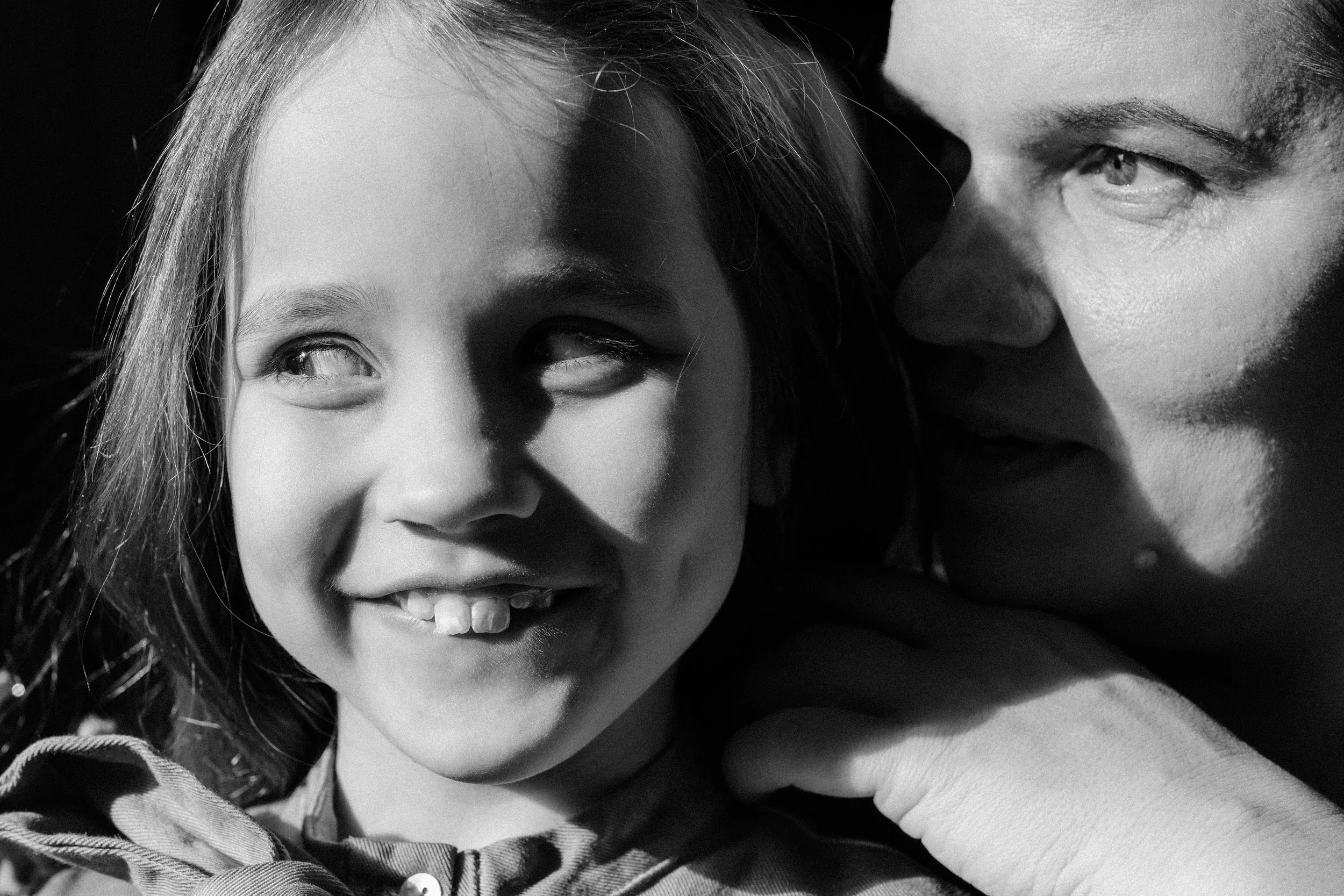 Close-up of a smiling young girl with a missing front tooth and a man whispering in her ear, both in black and white.