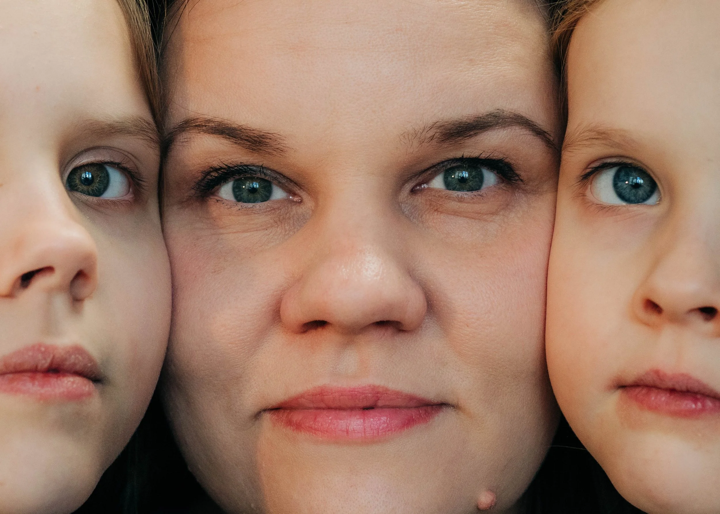 Close-up of a woman with two young children, all with blue eyes, faces close together, showing only part of their faces.