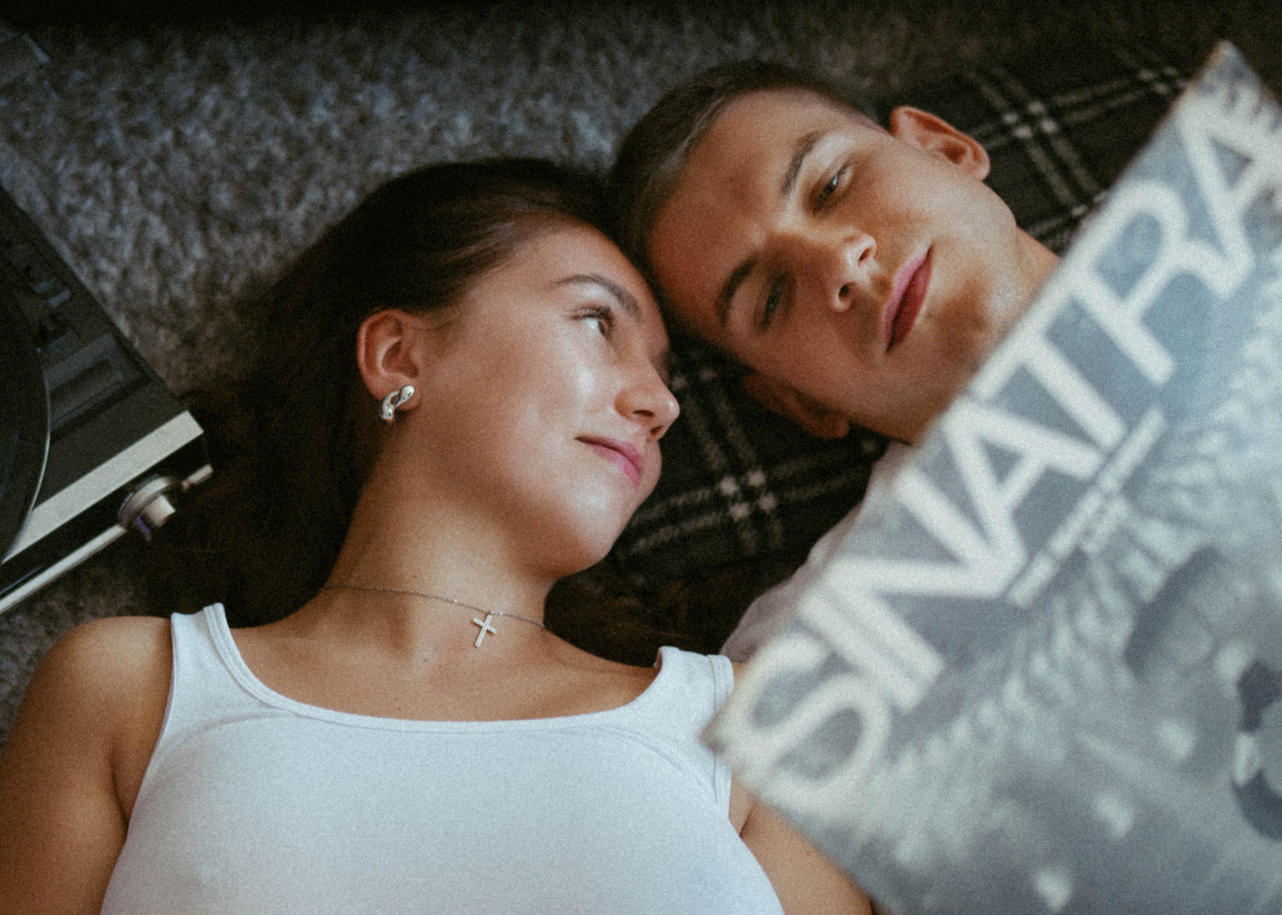 A woman and a man lying on the floor next to each other, possibly looking at a tablet.
