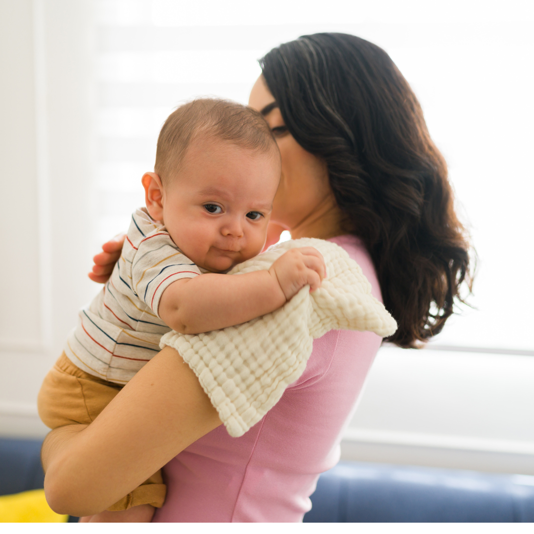 Mother in pink shirt holding a baby up on her shoulder to burp them
