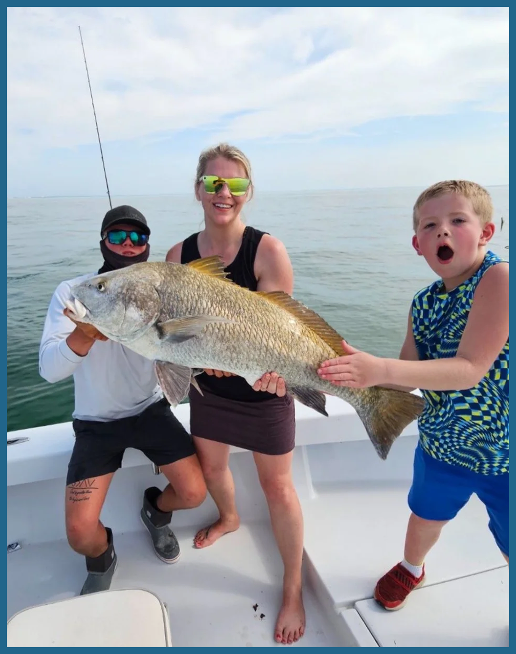 A fishing charter group holding a large redfish on a boat.