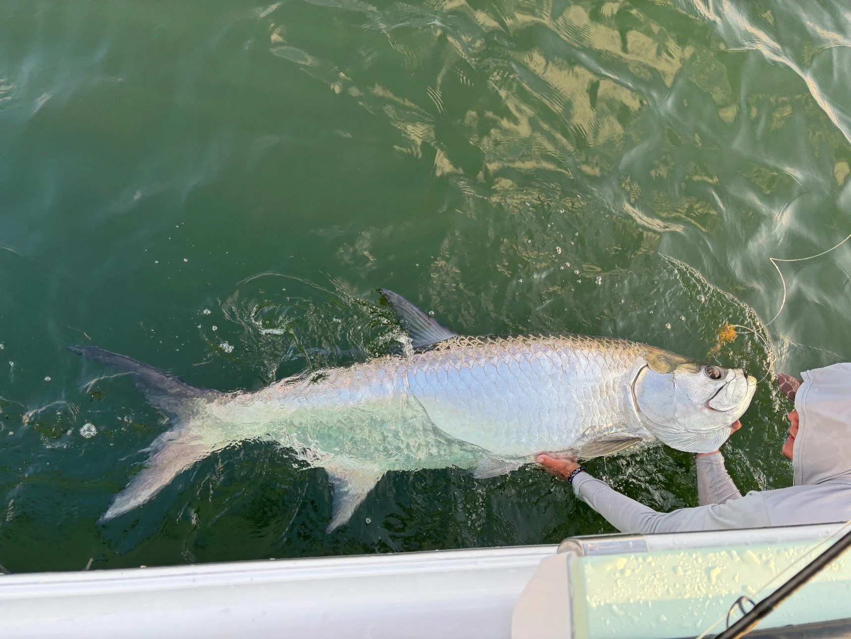A person steering a white center console boat on a lake, with a Yamaha outboard motor, surrounded by trees and cloudy sky.